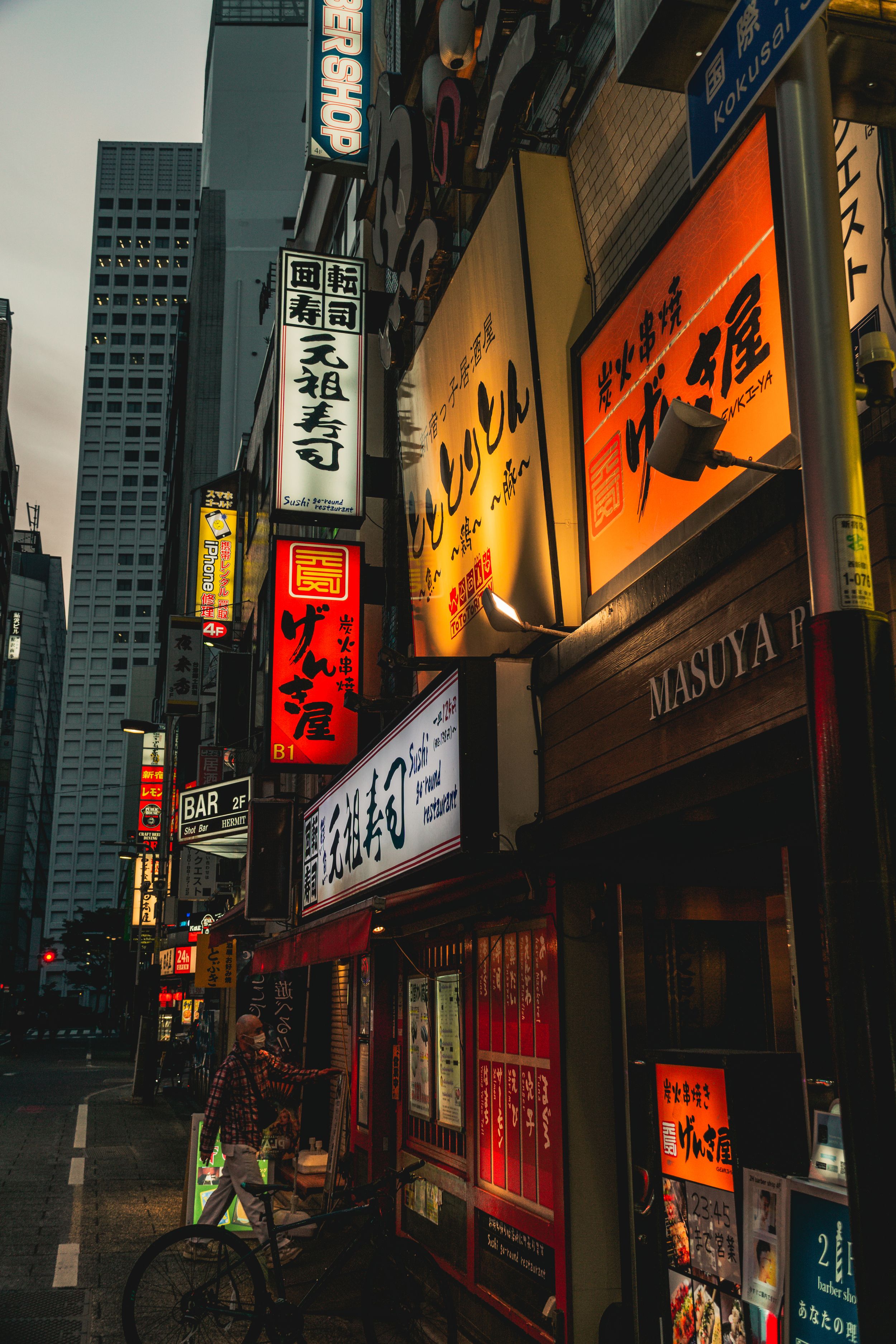 Neon signs and storefronts illuminate a narrow urban street in Japan at night with glowing orange and red hues.
