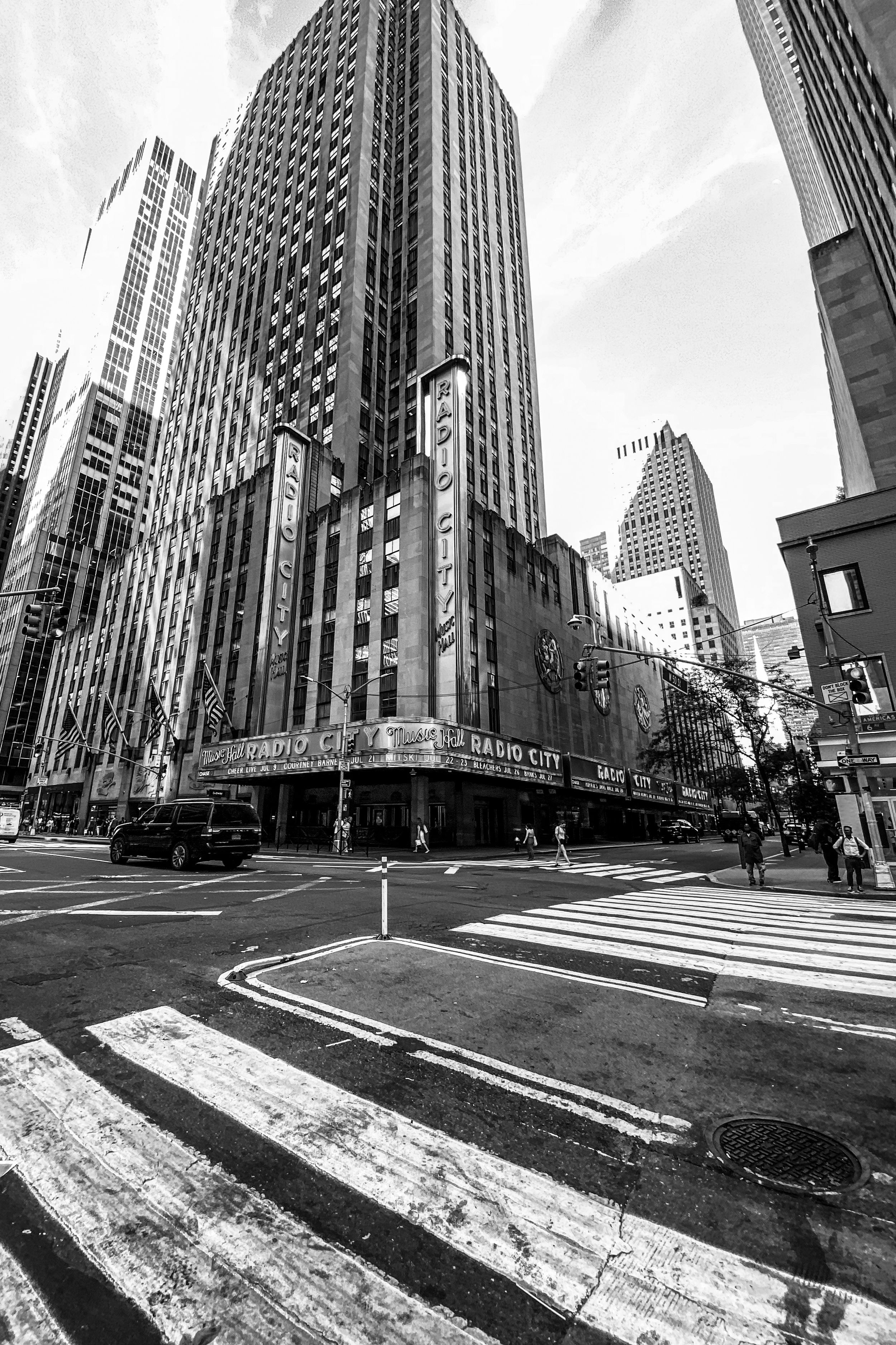 Tilted black and white urban street view showing a sequence of skyscrapers and crosswalk markings in Manhattan.