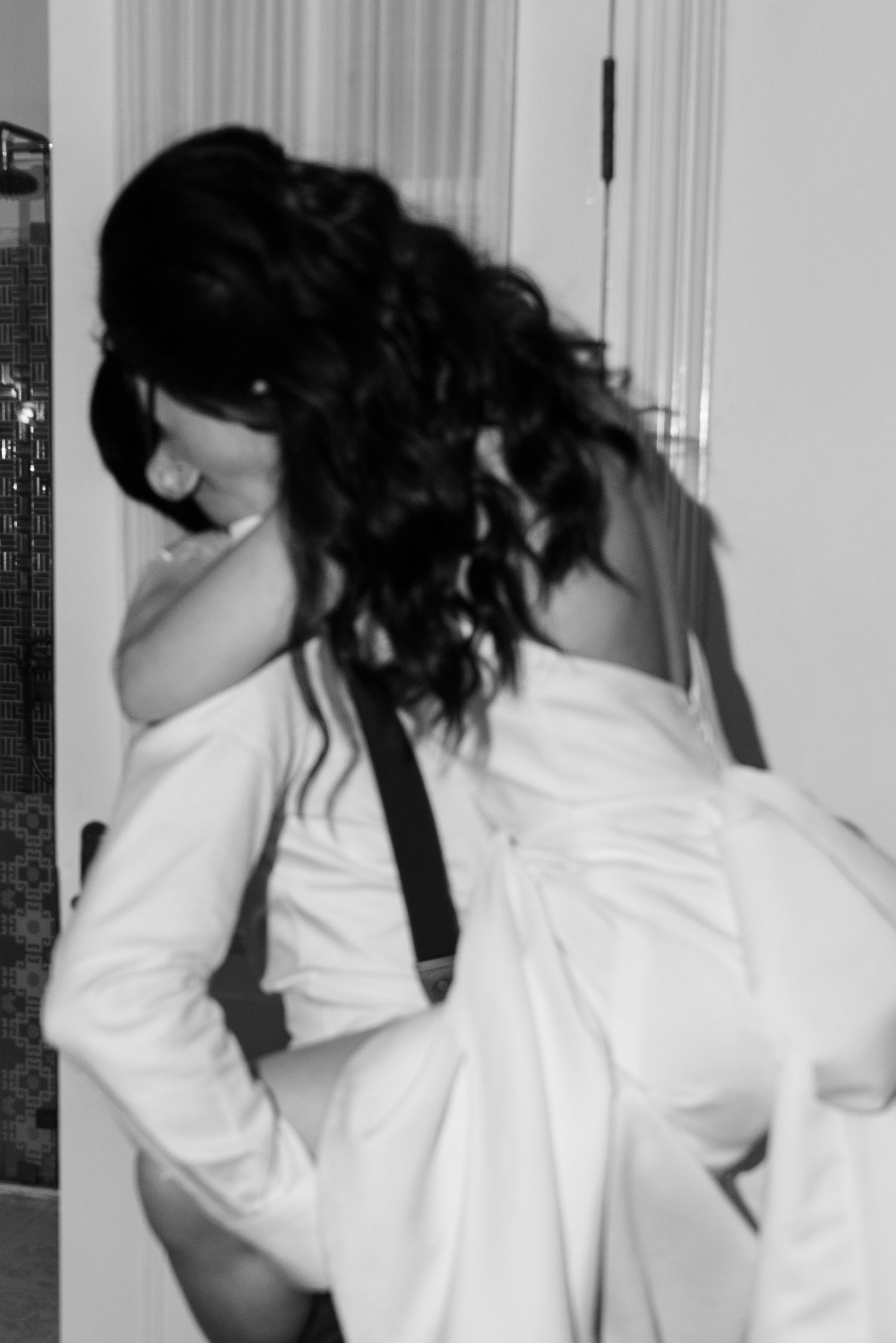 Black and white artistic photo of a woman with curly hair in a white shirt and suspenders.