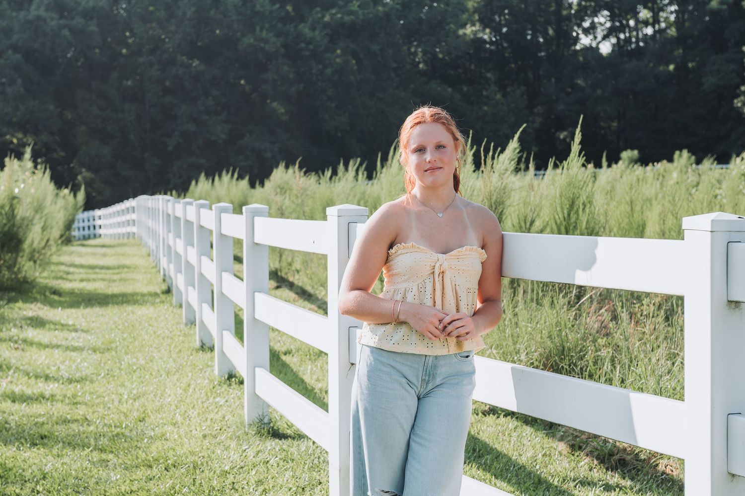 White wooden fence along a sunny grass field with a pastoral countryside setting.