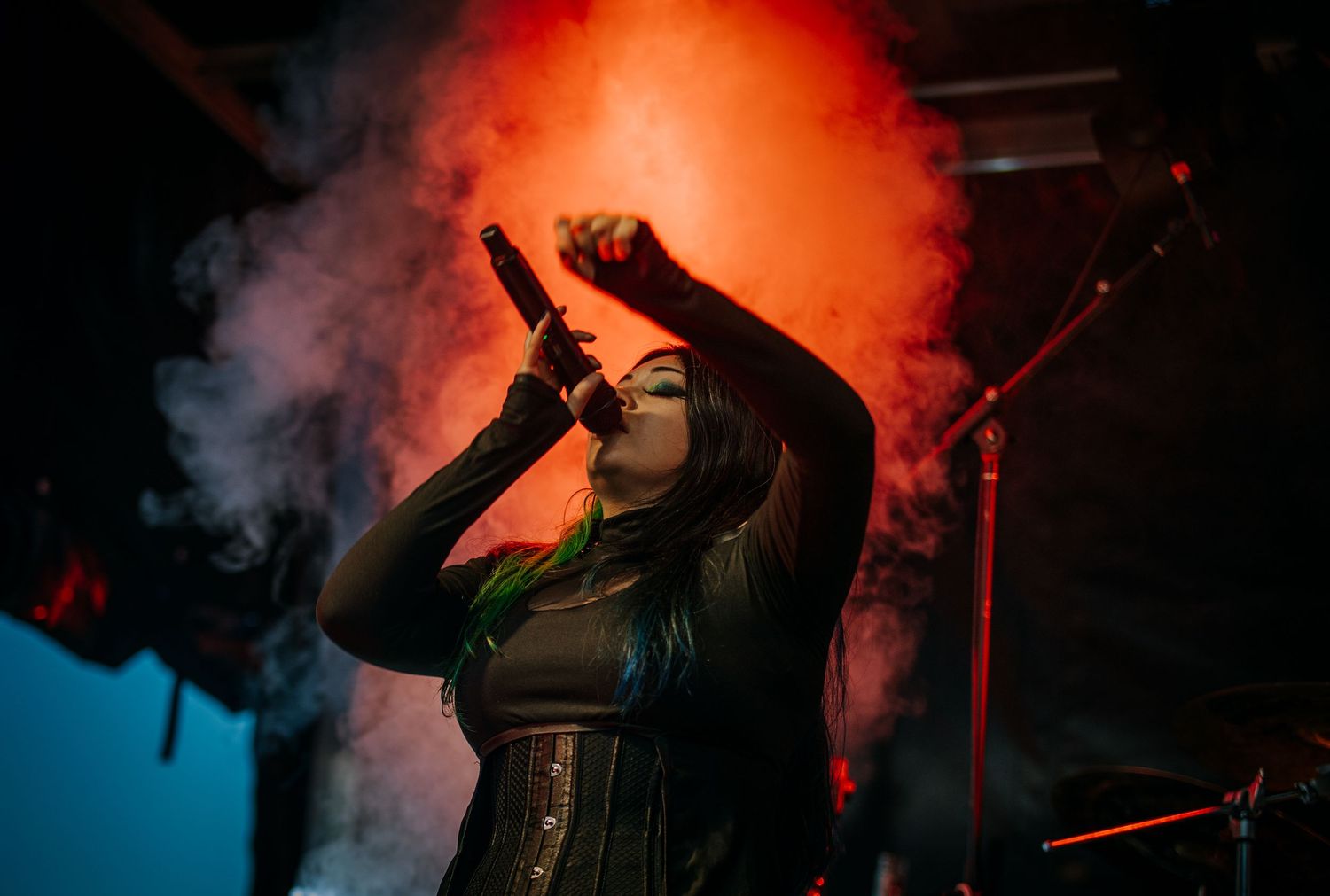A dramatic concert stage performance with red smoke effects and dynamic lighting illuminating the performers against a dark backdrop.