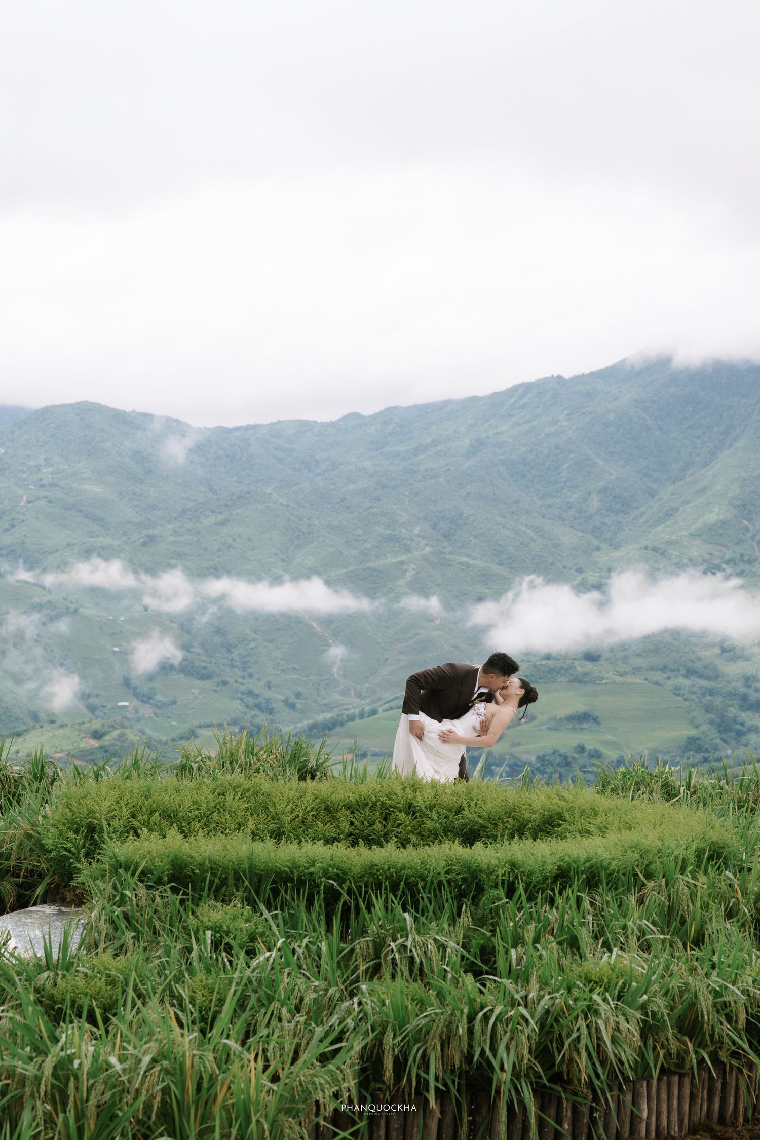 Couple sharing a romantic kiss on a green hilltop with stunning misty mountain valley views in the background.