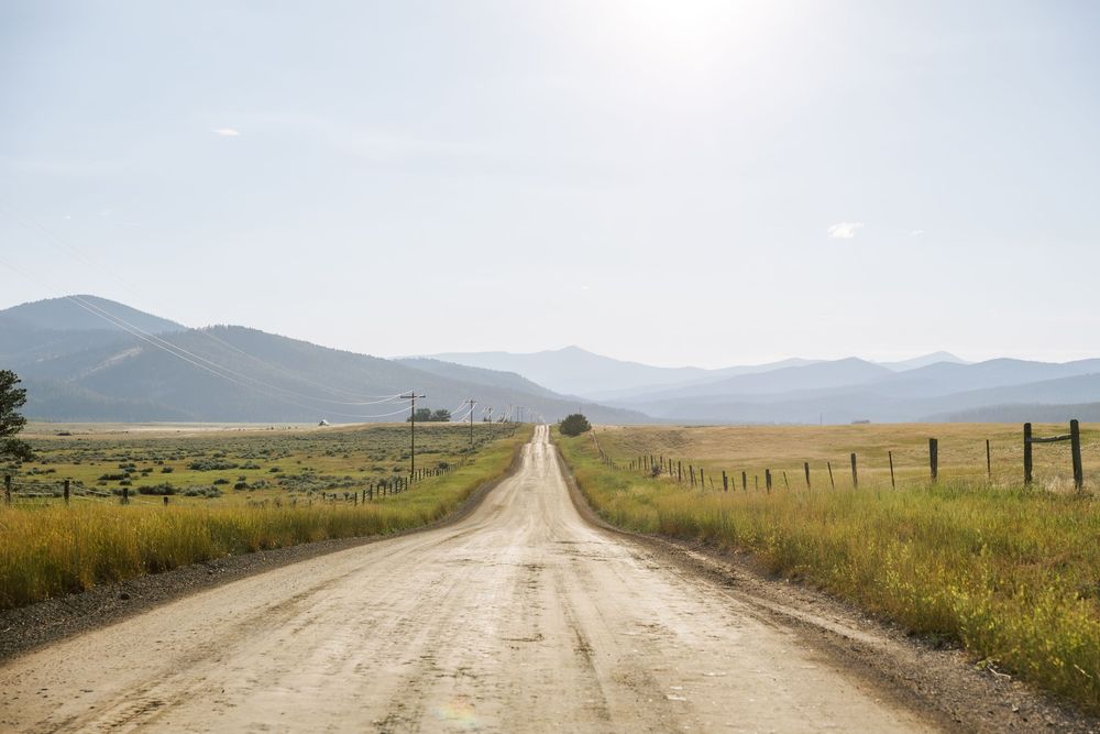 Panoramic view of a long dirt road stretching through rural mountain landscape.