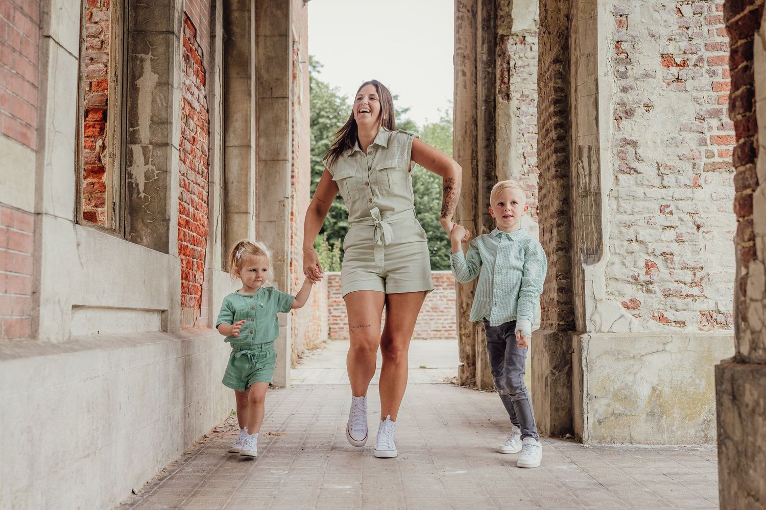 Family walks through historic brick archways in coordinating mint green and white outfits during outdoor photo session.