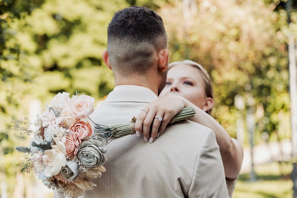 A couple shares a tender embrace during an outdoor autumn wedding ceremony with soft pink floral decorations.