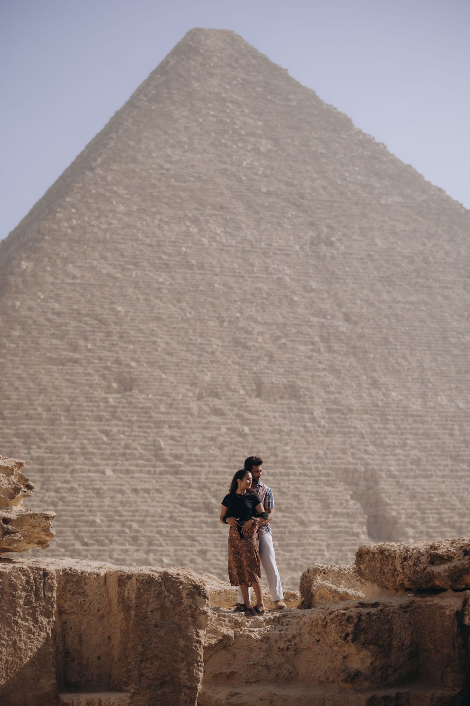 Tourist standing near massive ancient Egyptian pyramid stone blocks in desert landscape.