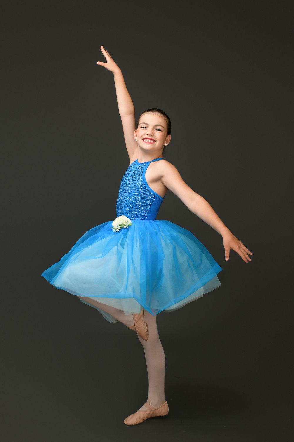 Young dancer in bright blue tutu dress practices ballet moves against dark background in progressive motion sequence.