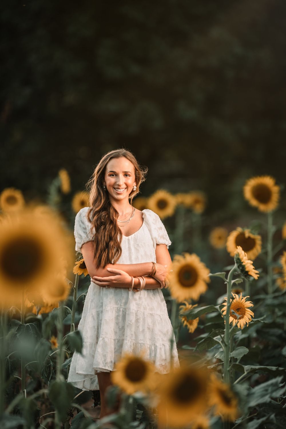 A white dress stands out among vibrant yellow sunflowers in a scenic summer field during golden hour.