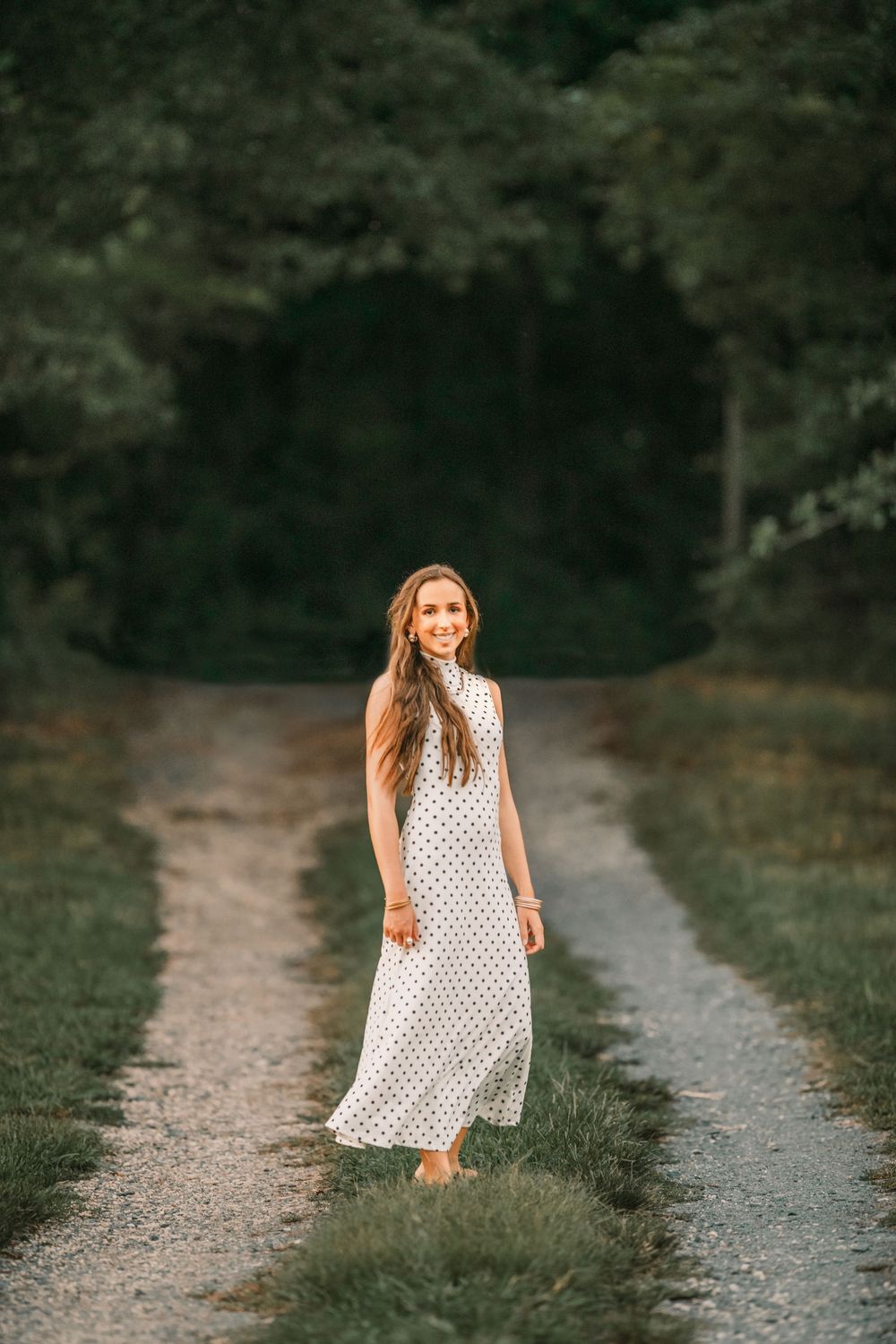 A polka dot summer dress flows gracefully along a winding dirt path through a lush green forest setting.
