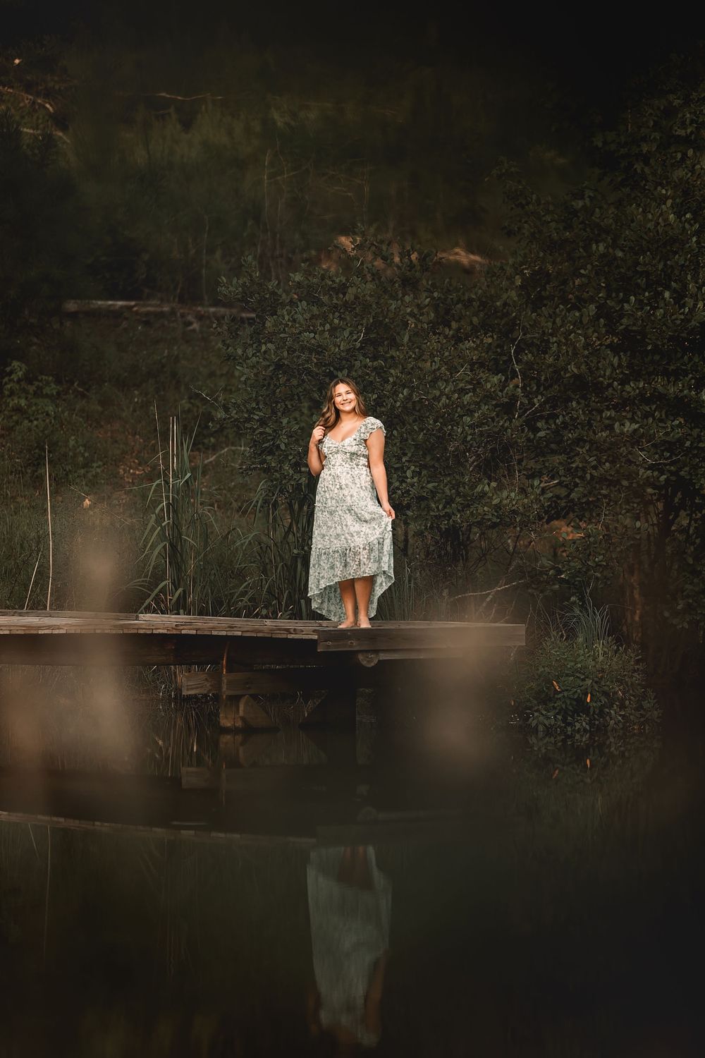 A white dress on a wooden dock surrounded by misty water and forest foliage at sunset.