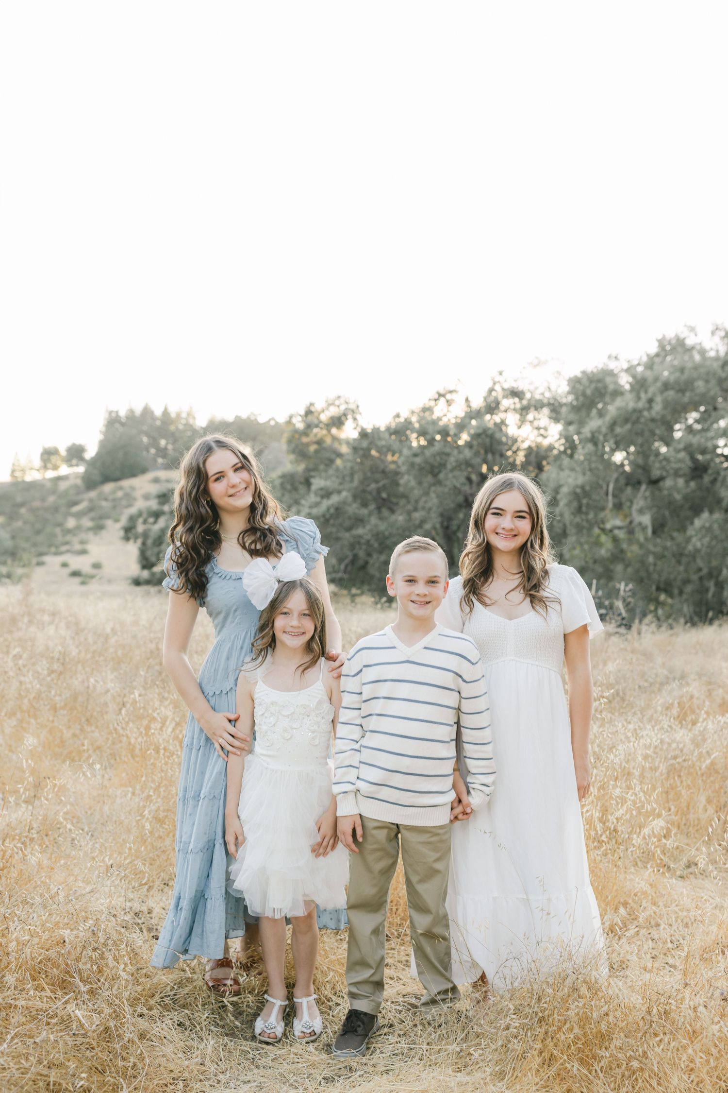 Family wearing coordinated white and blue outfits poses together in golden grassy field during sunset photoshootcaptured by Chelsee Rawe Ph.