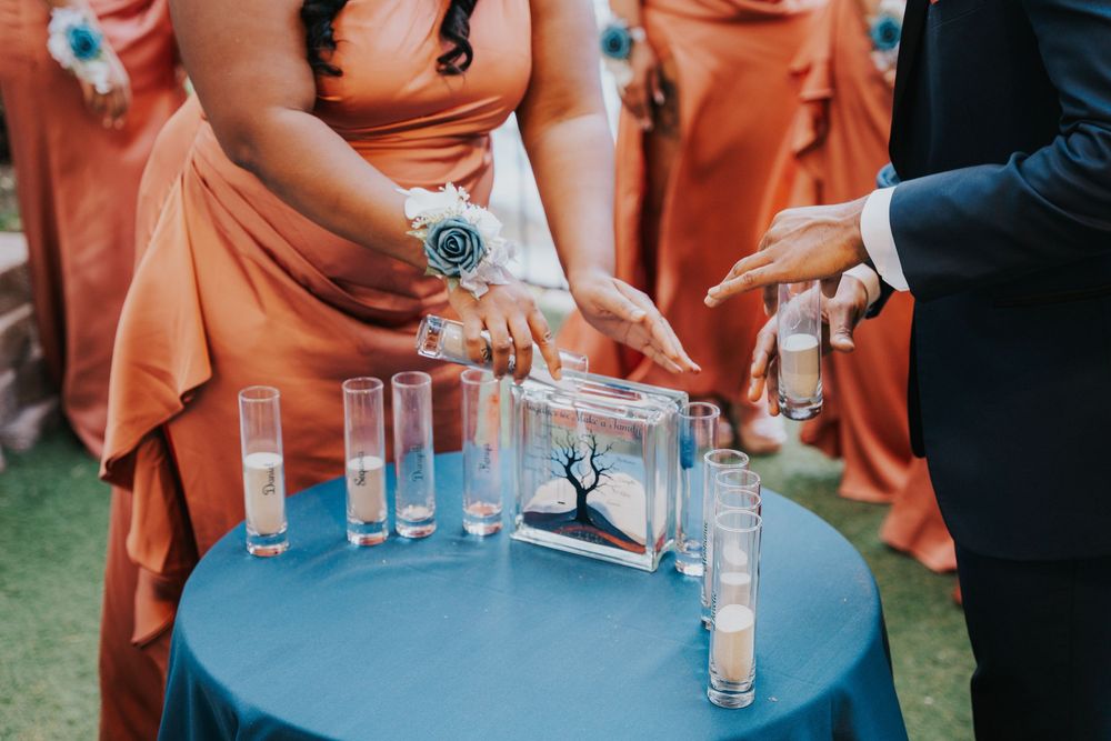 Wedding party members in coral-colored dresses gather around a blue cocktail table with drinks.