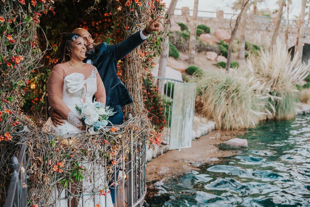 Wedding couple embraces near water fountain in lush garden setting at tropical resort venue at sunset.