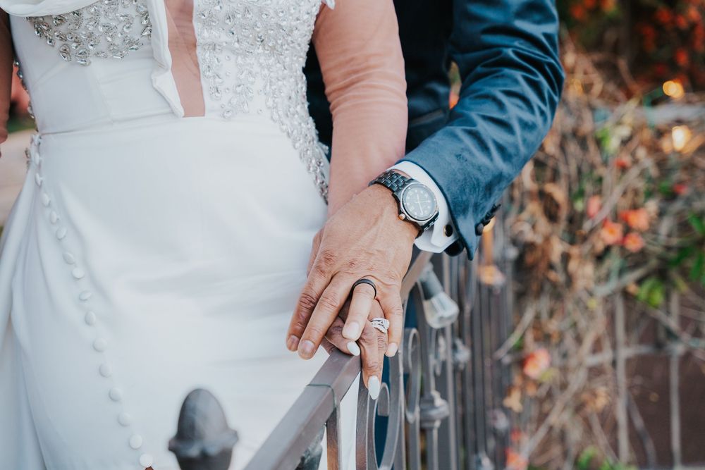 Close-up shot of wedding attire details showing a white lace dress and blue sleeve with hands resting on a railing.