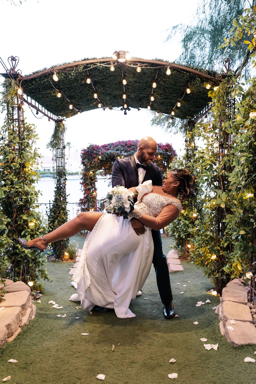 Romantic dip sequence at an outdoor wedding with string lights and floral arch in a garden setting.