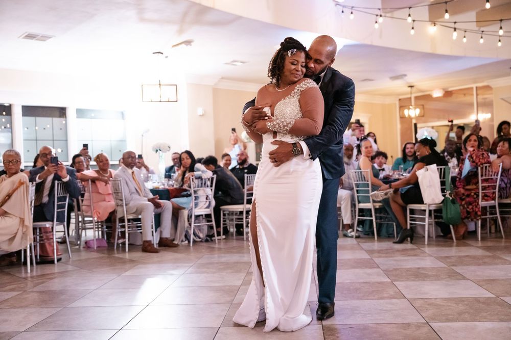 A couple shares their first dance at their wedding reception while guests watch from decorated tables in a banquet hall.