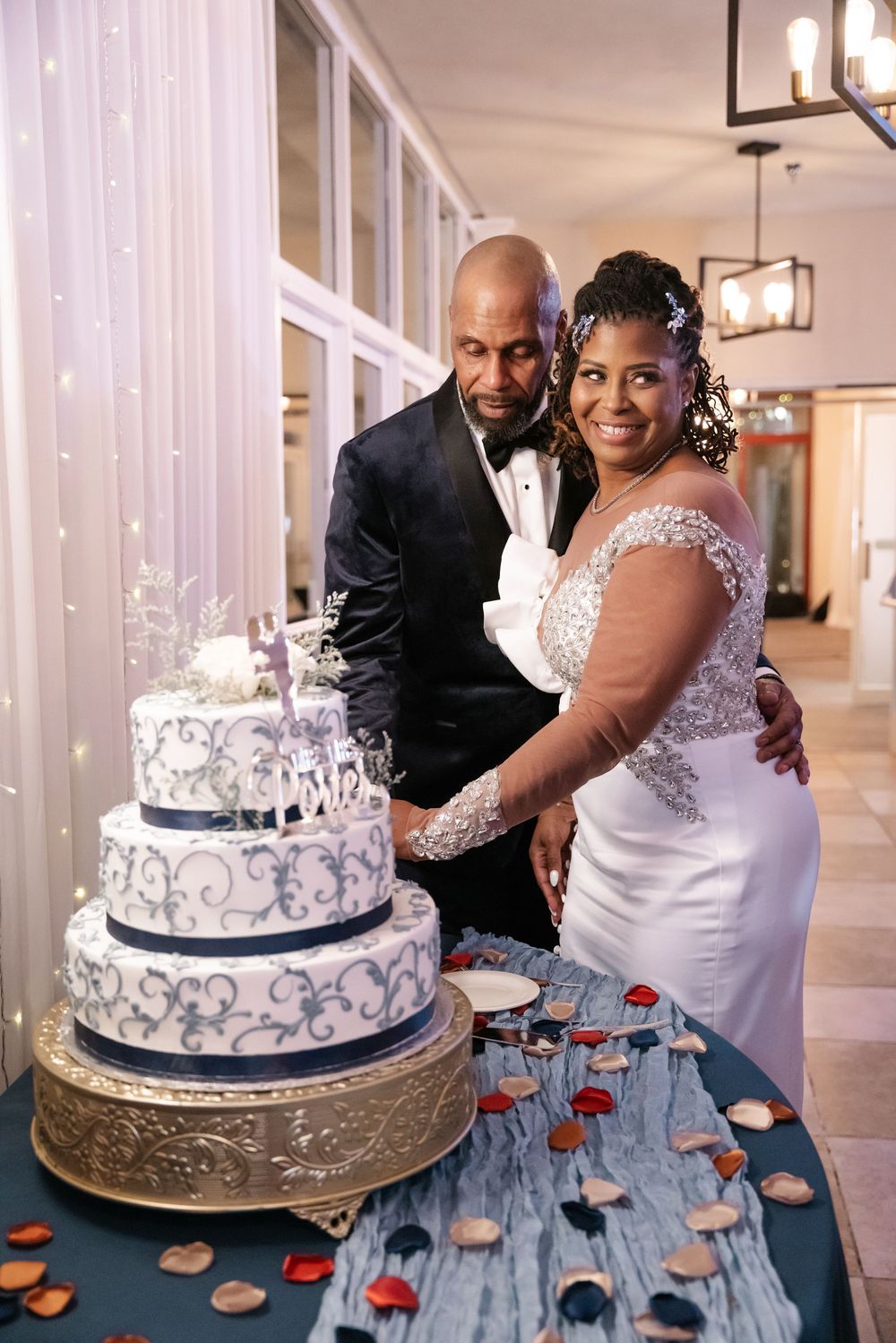 Wedding couple cuts into an elegant white and silver wedding cake with blue scrollwork details at their reception celebration.