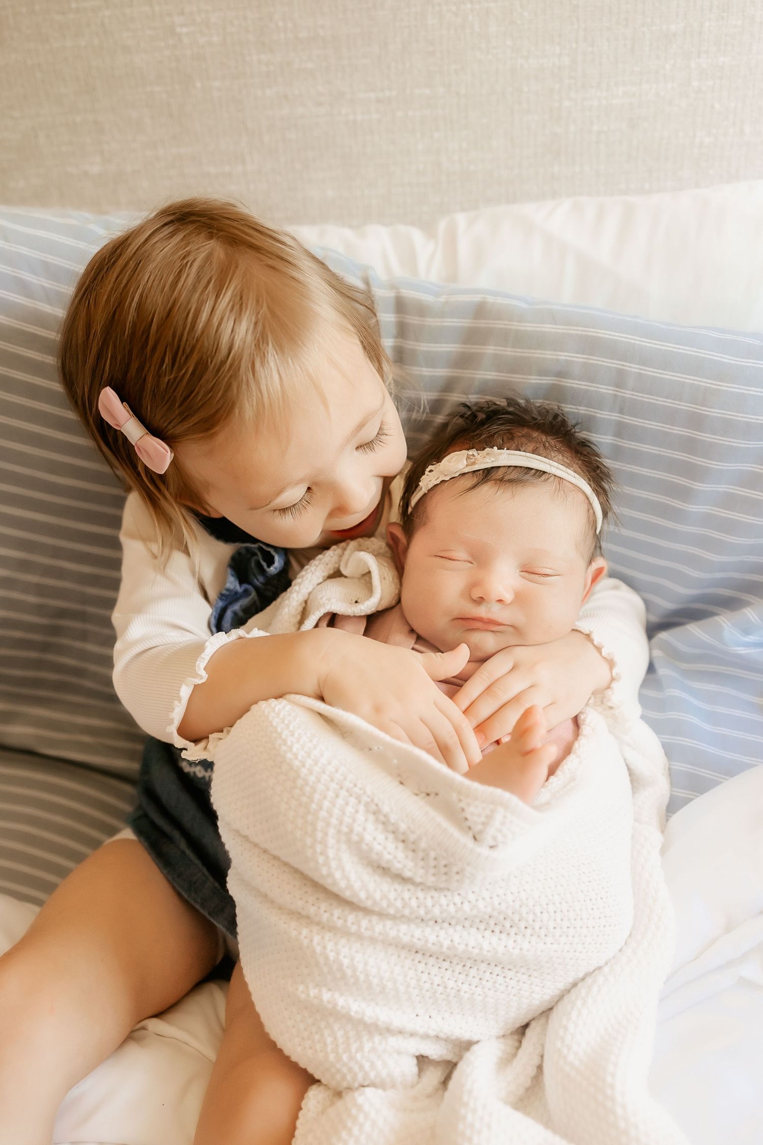 A little girl holds her newborn baby sister as an Oahu Newborn Photographer captures their snuggle during their newborn photo session.