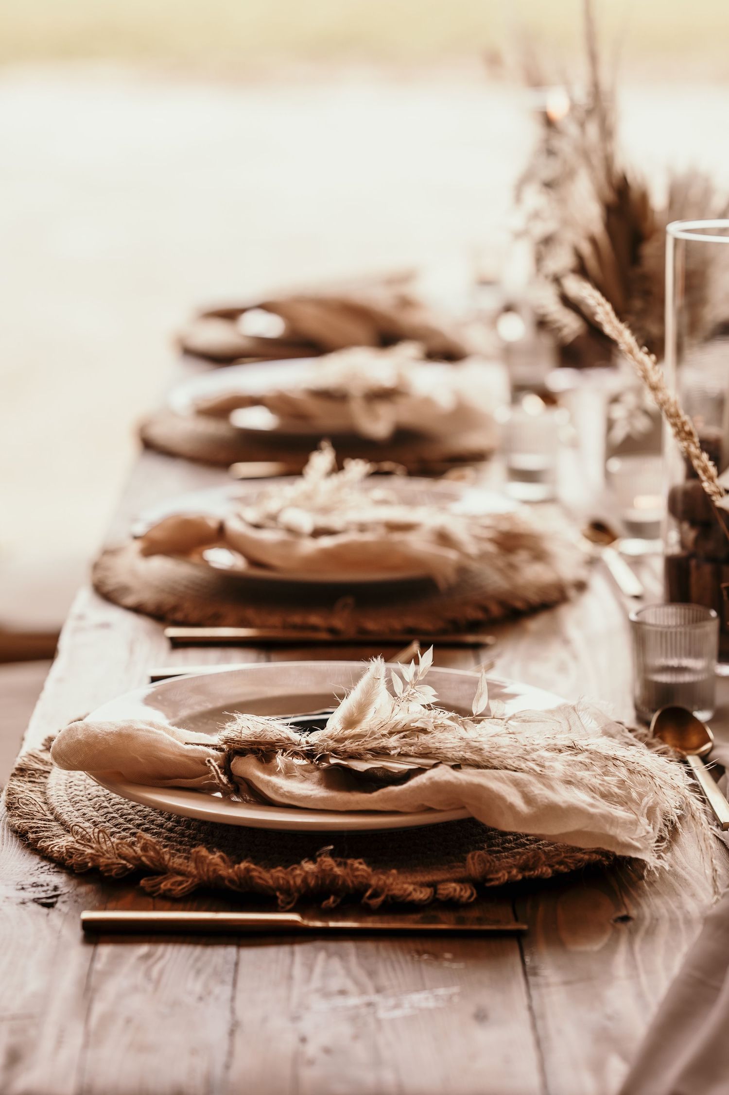 A rustic table setting with brown ceramic plates and dried floral accents in a sepia-toned photograph.