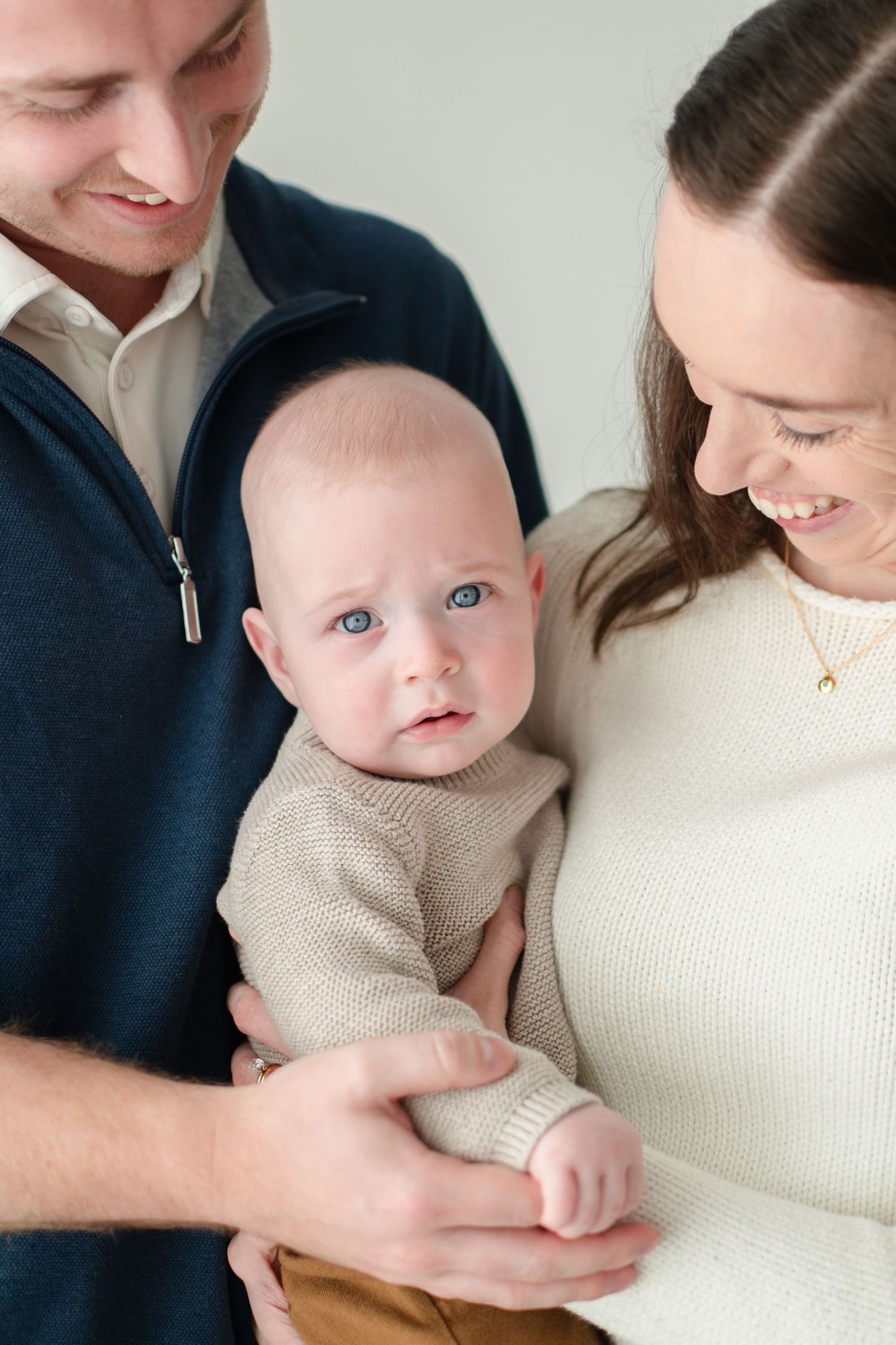 Parents in navy and cream sweaters hold their infant in beige knit, capturing tender family moments in a series of candid shots.