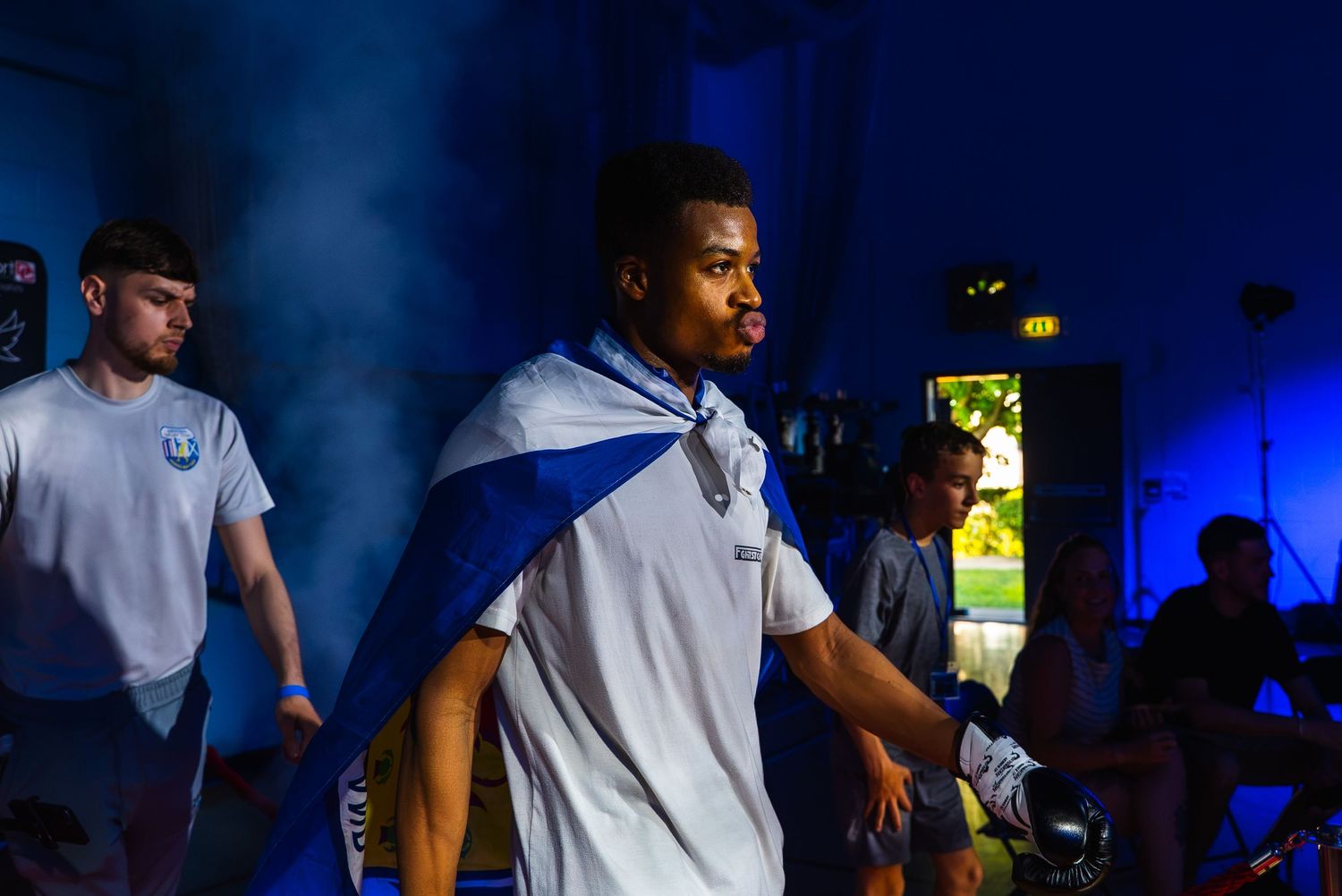 Athletes in blue and white capes walk through dramatic blue smoke during a sporting event entrance.