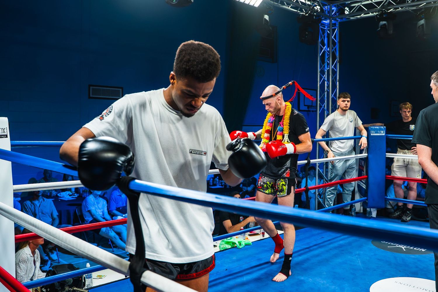 Two boxers training in a blue boxing ring during a sparring session at an indoor boxing gym.