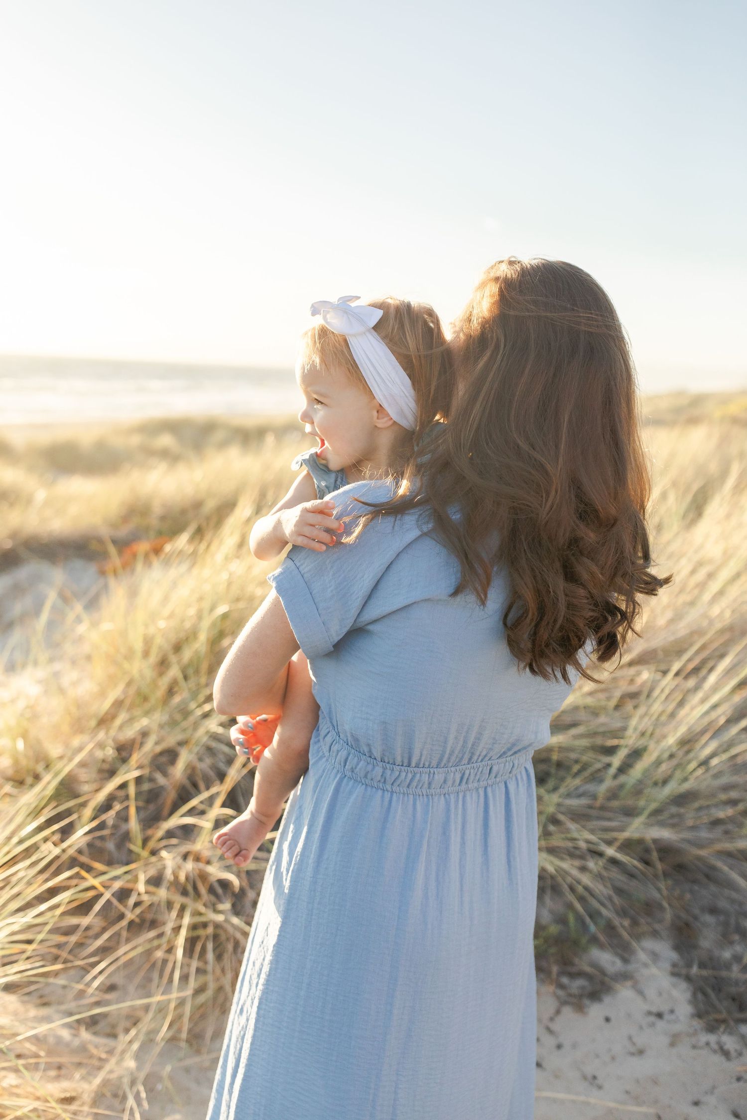 Young girl in light blue dress walking through golden beach grass during sunset.Film by Chelsee Rawe Photography