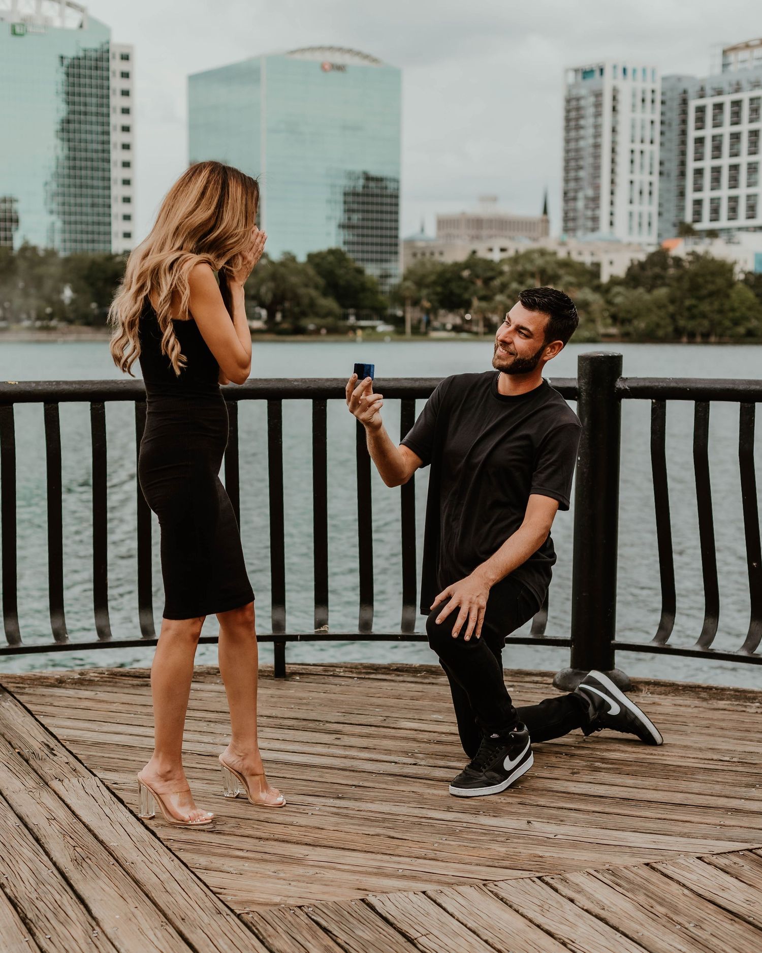 Romantic couple interaction on wooden pier with city skyline backdrop.