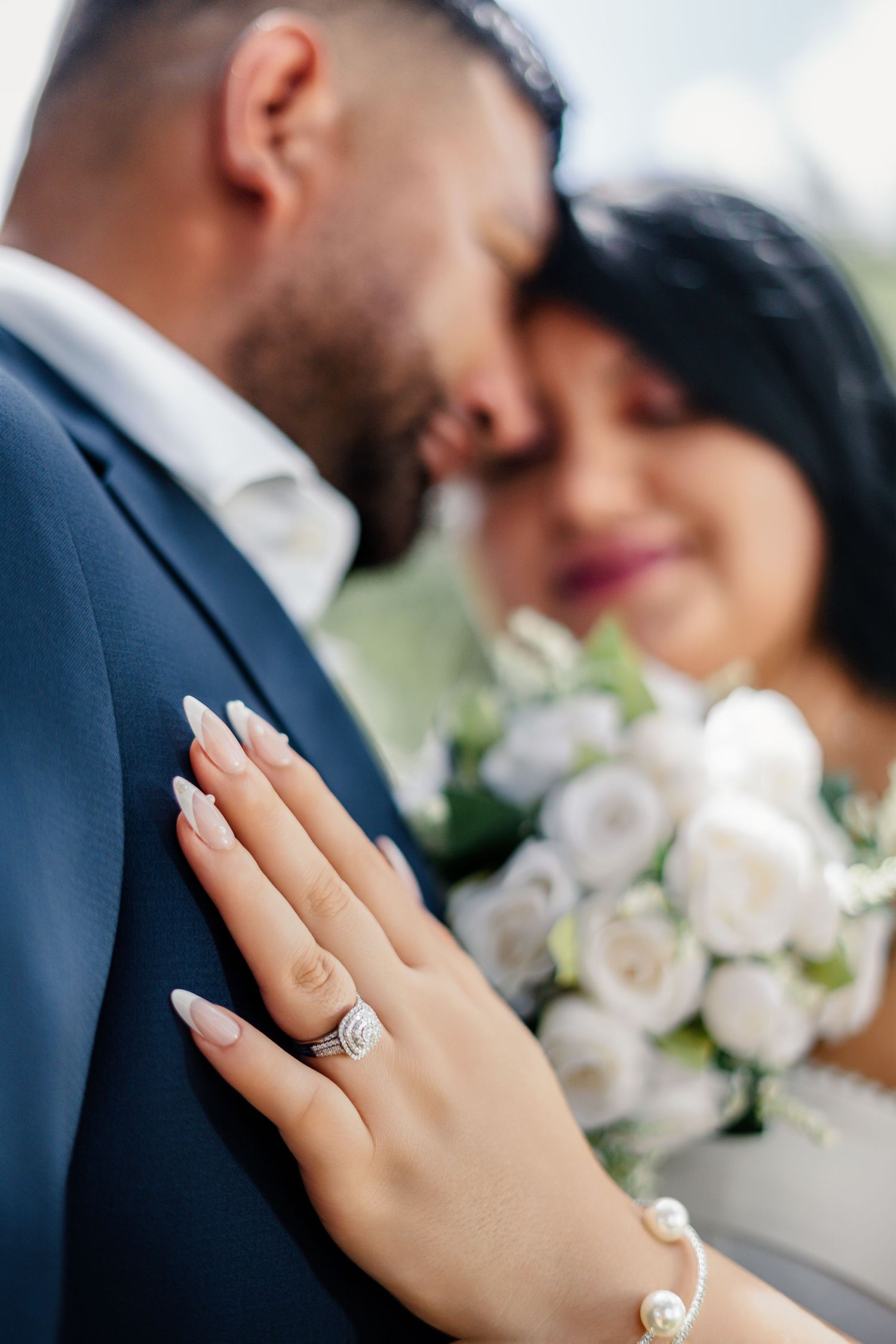 Close-up of couple showing engagement ring with white roses bouquet.