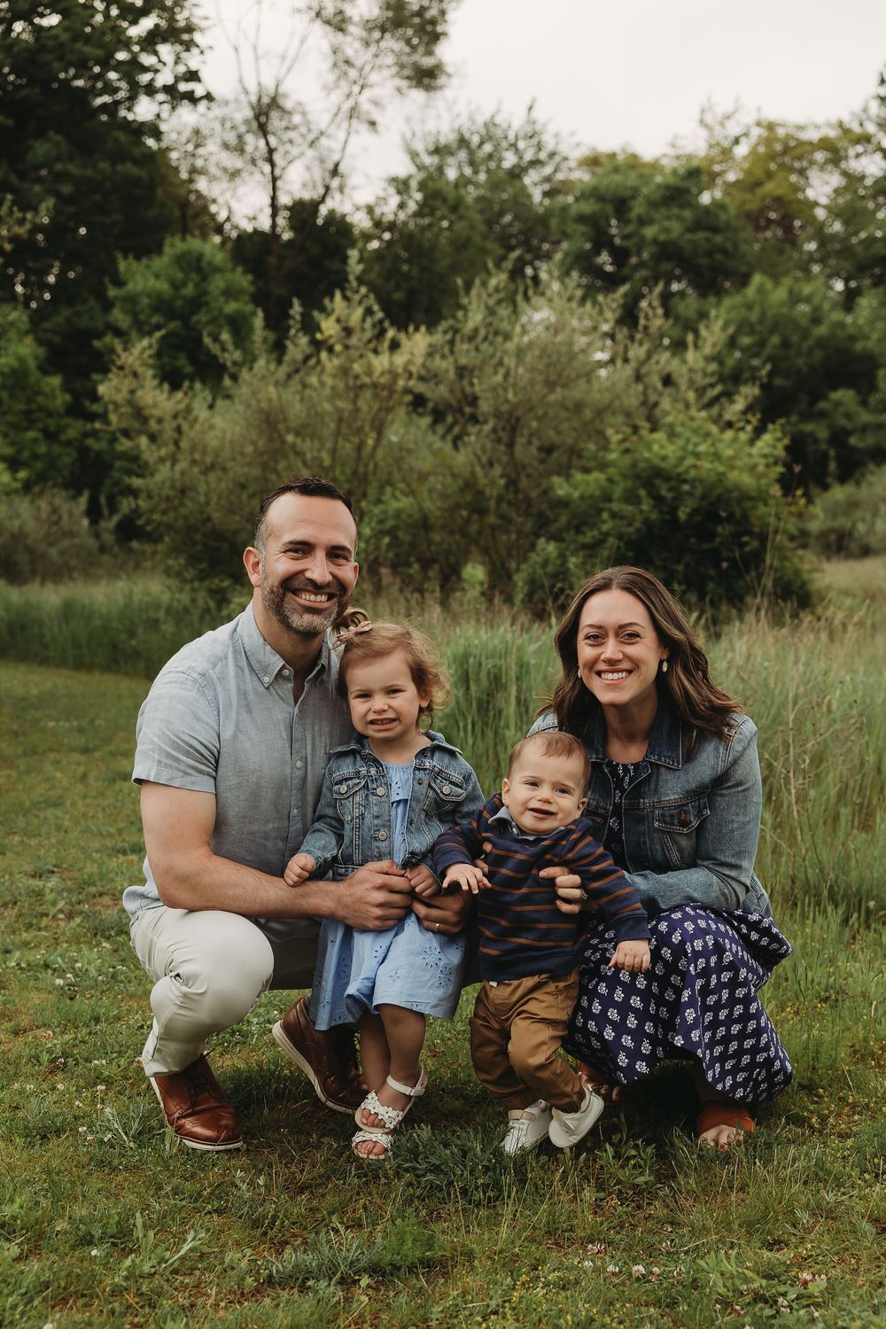 A happy outdoor family portrait showing joyful expressions while sitting together in a natural setting with tall grass.
