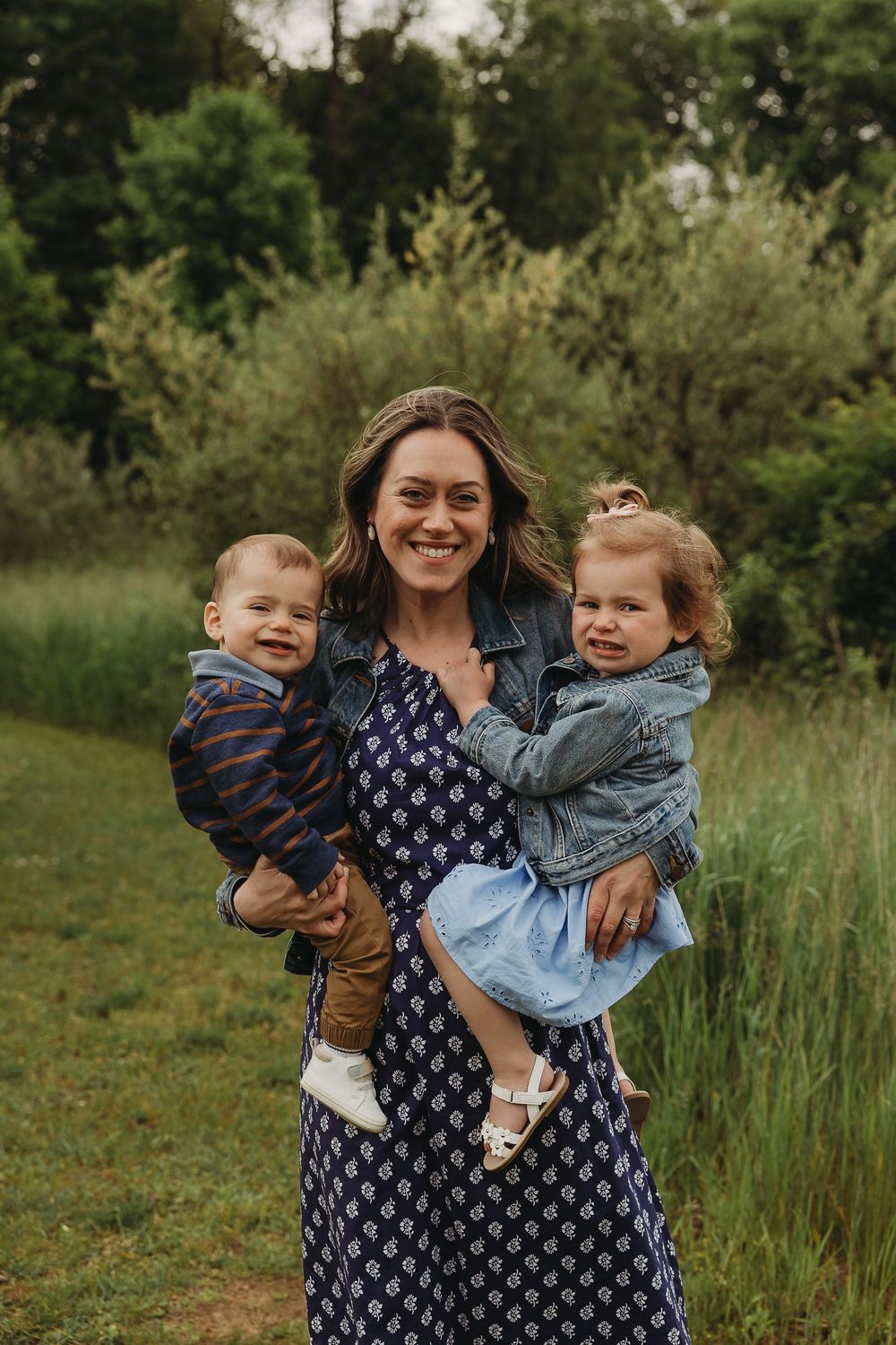 A joyful outdoor family portrait in a natural field setting with lush greenery in the background.