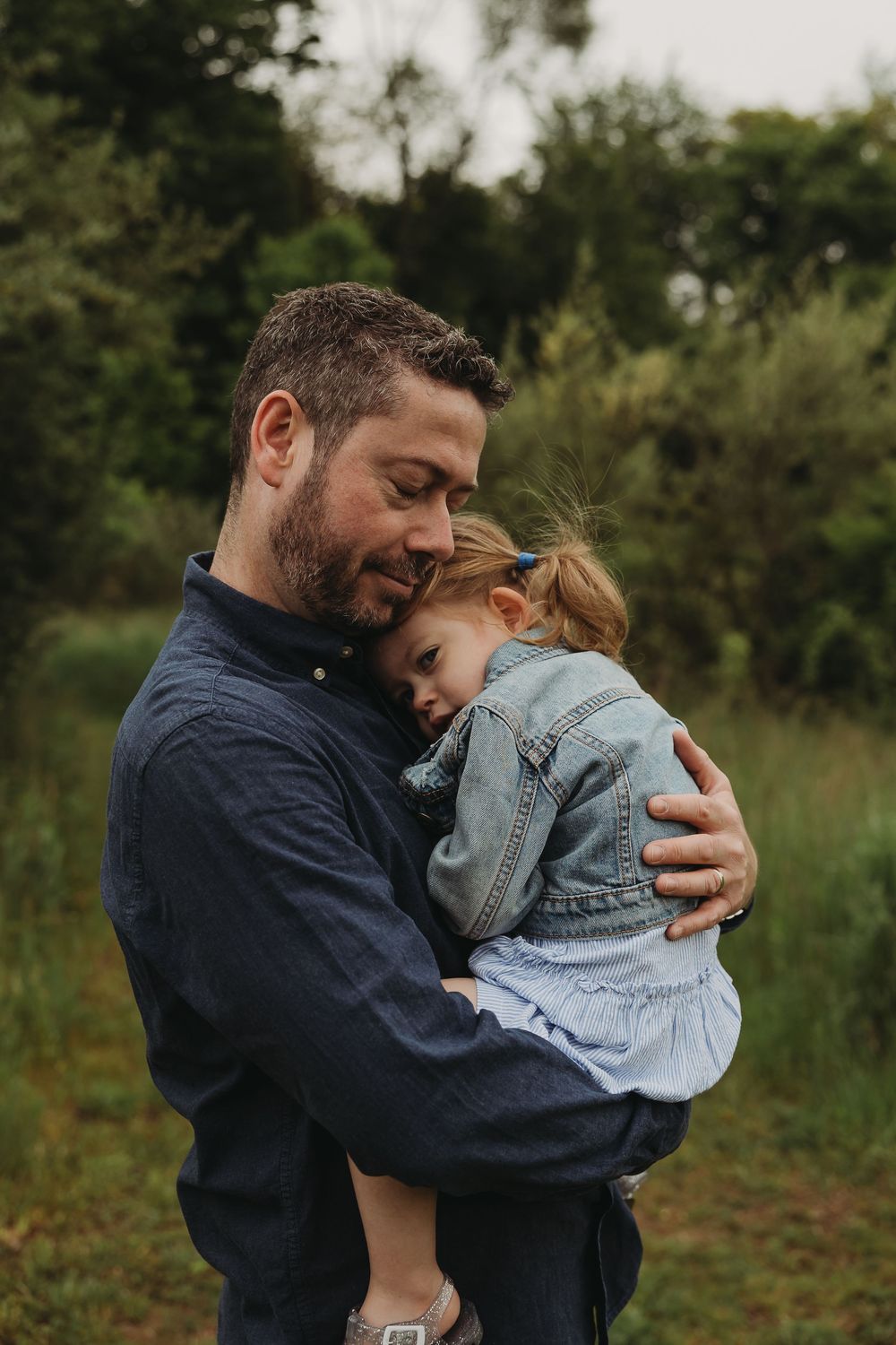 A tender outdoor moment shows an embrace between an adult in navy blue and a small child in denim.