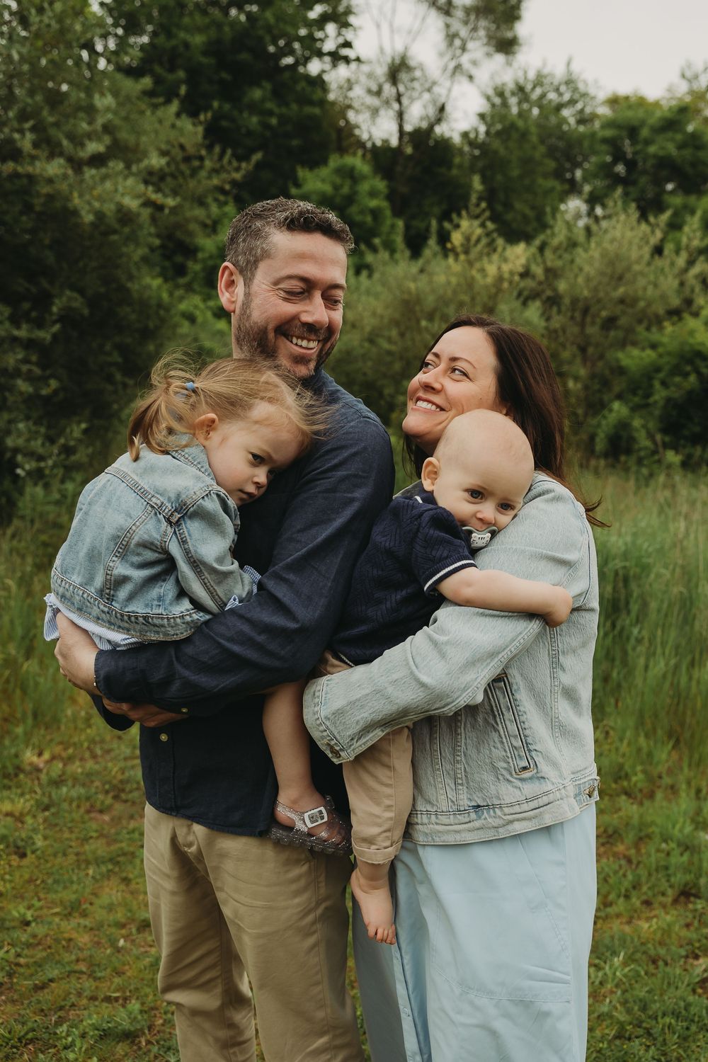 A joyful family shares laughter and embraces while standing together in a lush green outdoor setting.