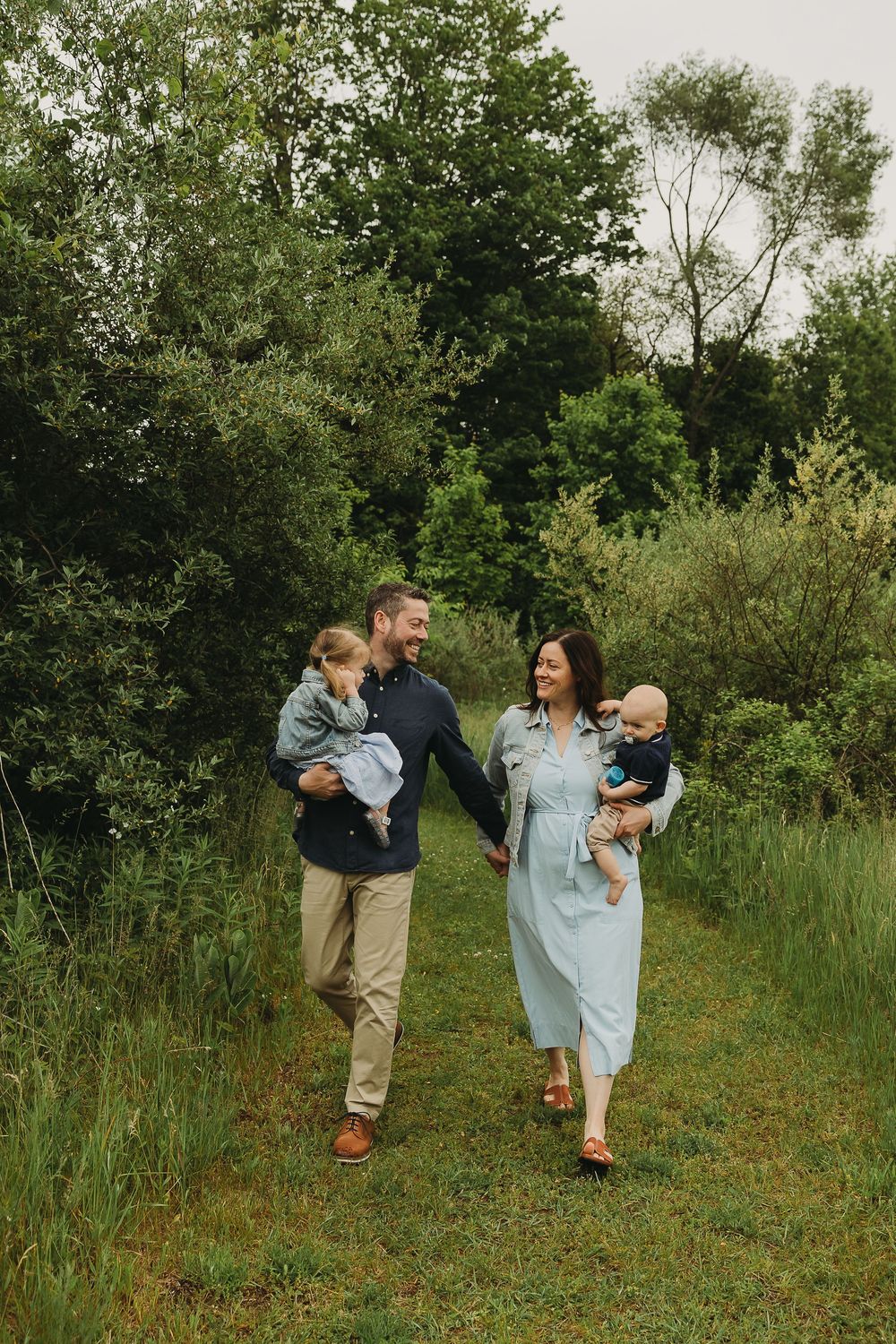 A family walks together on a scenic trail surrounded by lush green trees and vegetation.