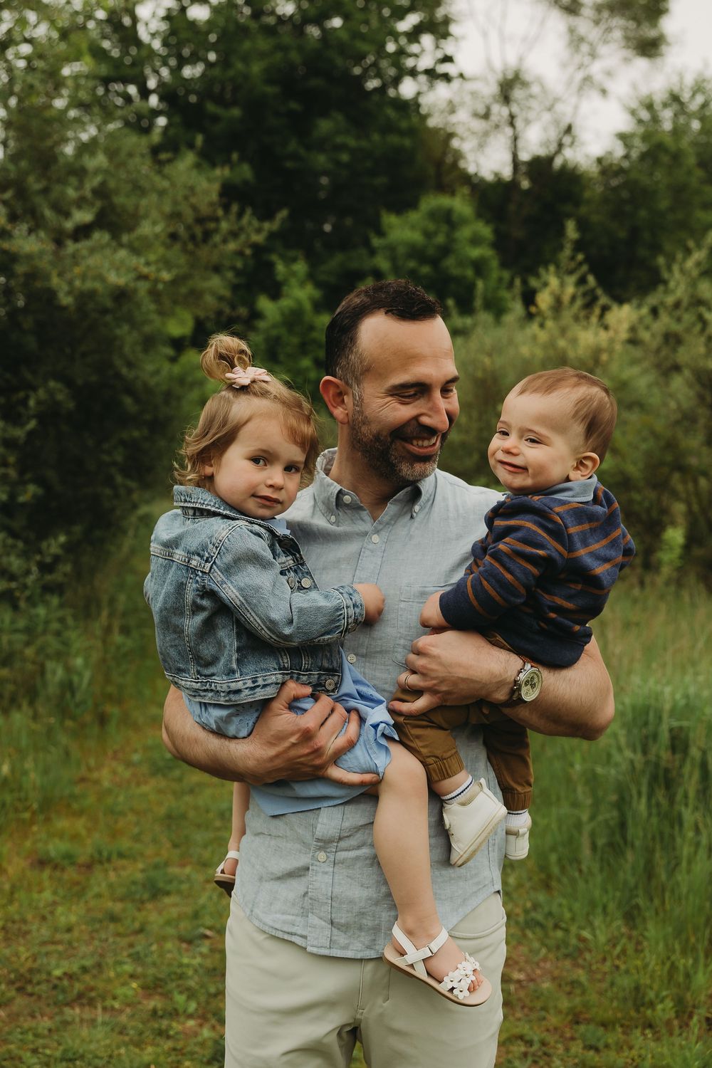 A joyful outdoor family moment captured in a natural setting with greenery in the background during summer.