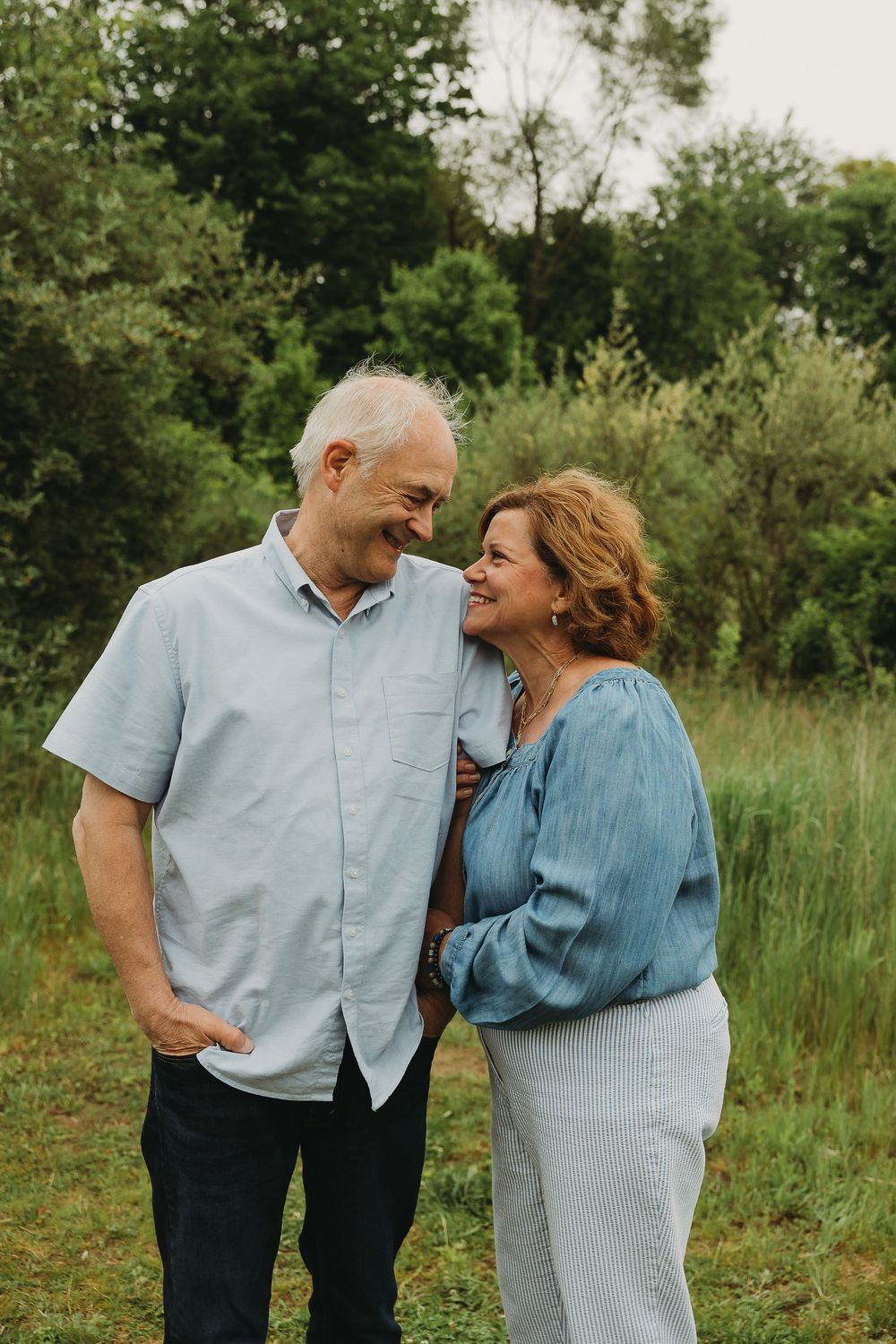 A couple sharing tender moments and laughter together in a grassy outdoor setting.