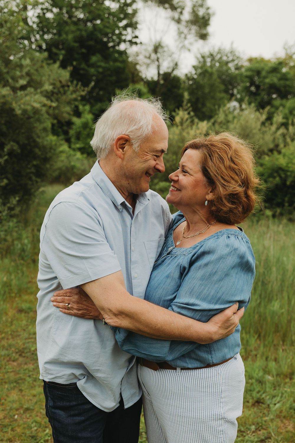 Mature couple sharing a tender moment while embracing outdoors in a natural setting with green foliage.