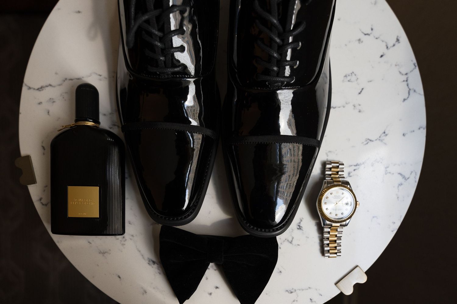 Overhead view of black leather dress shoes displayed on white marble surface with watch and perfume bottle. Chicago wedding photographer