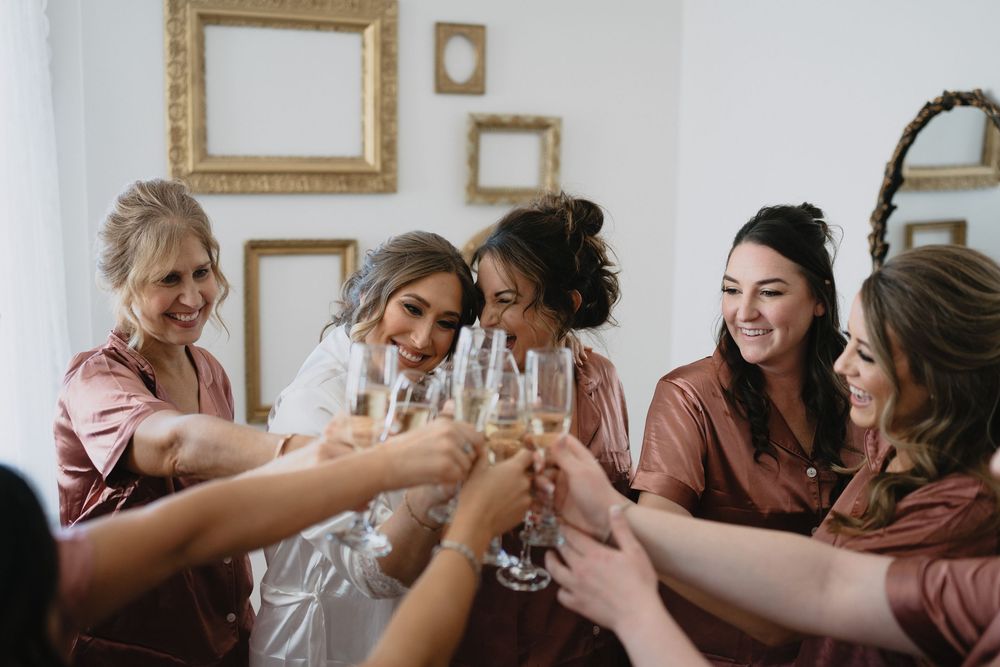 Bride and bridesmaids in matching robes toasting with champagne glasses during wedding morning preparations. Manor House Colorado
