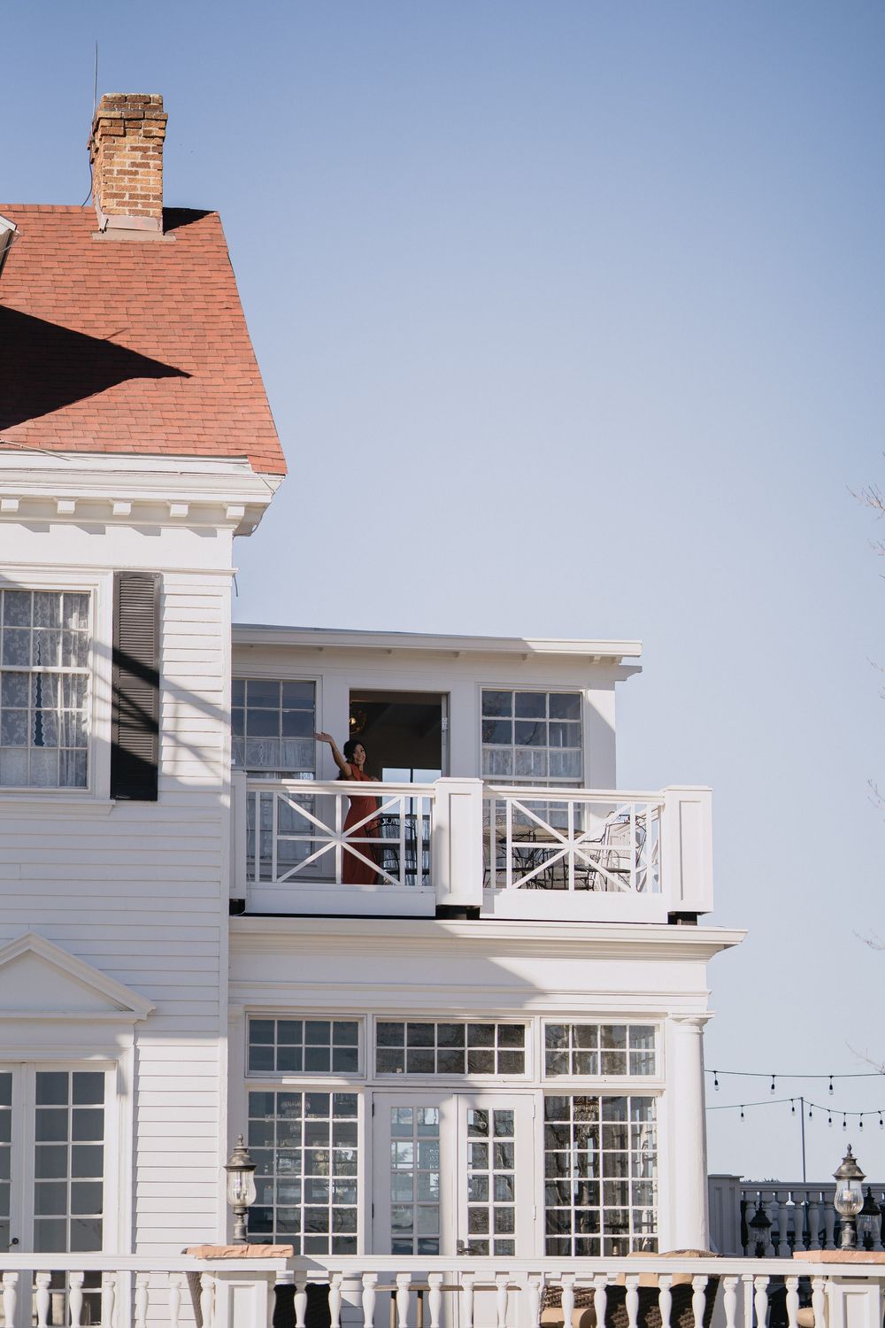 White coastal building with balcony, large windows, red roof, and chimney against a clear blue sky.