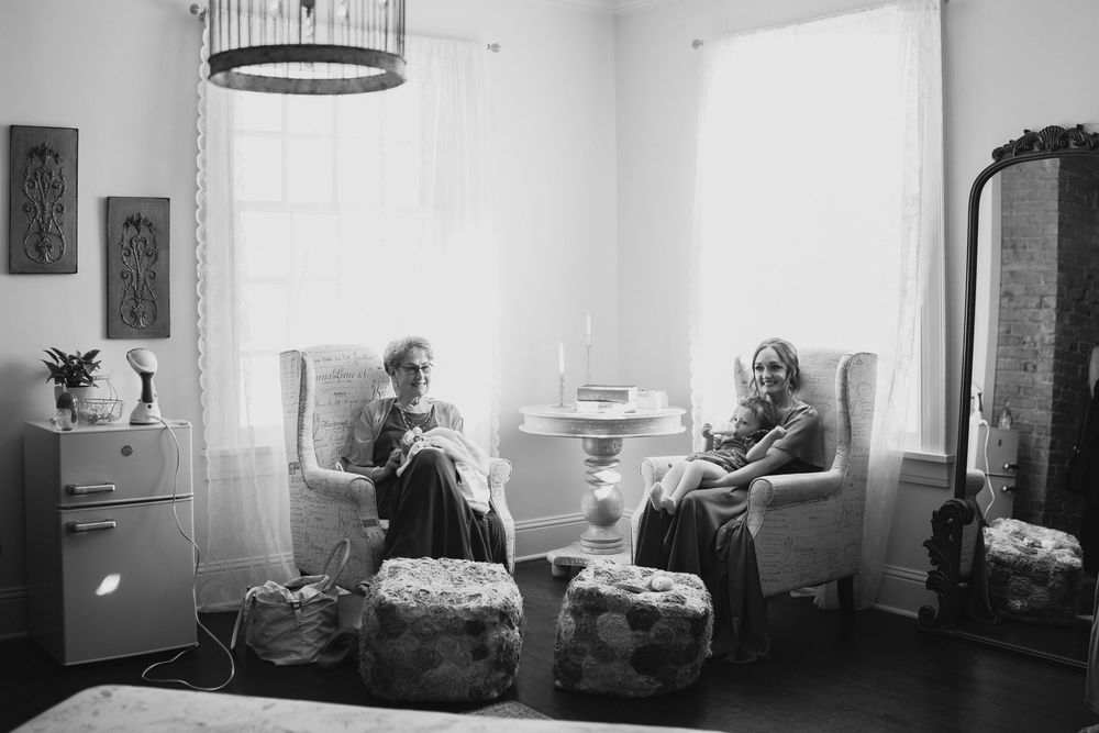 Two women sit in wingback chairs by bright windows in a cozy room, captured in black and white photography.