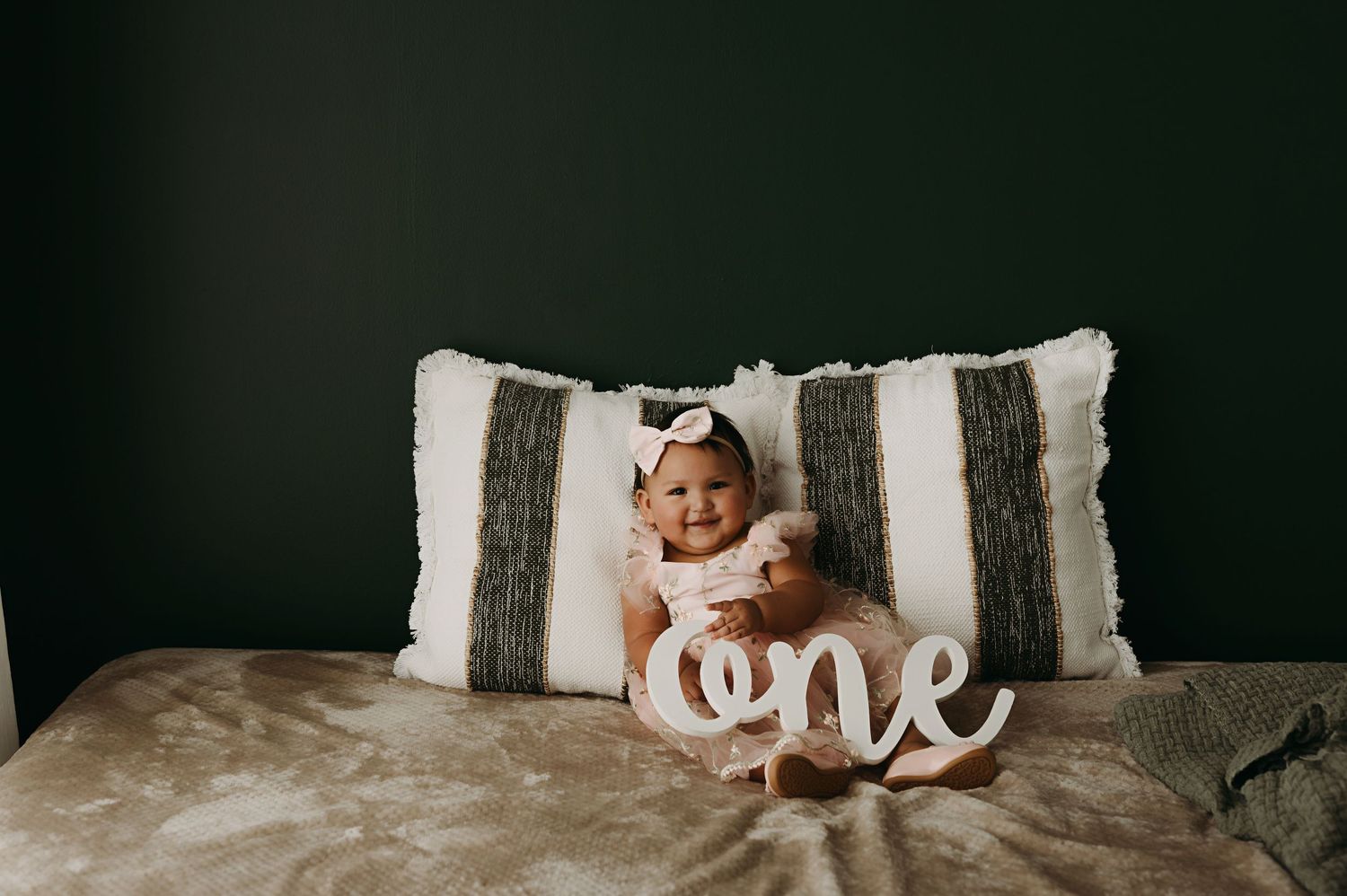 Baby bedroom features a soft teddy bear and decorative 'one' text sign on white bedding.