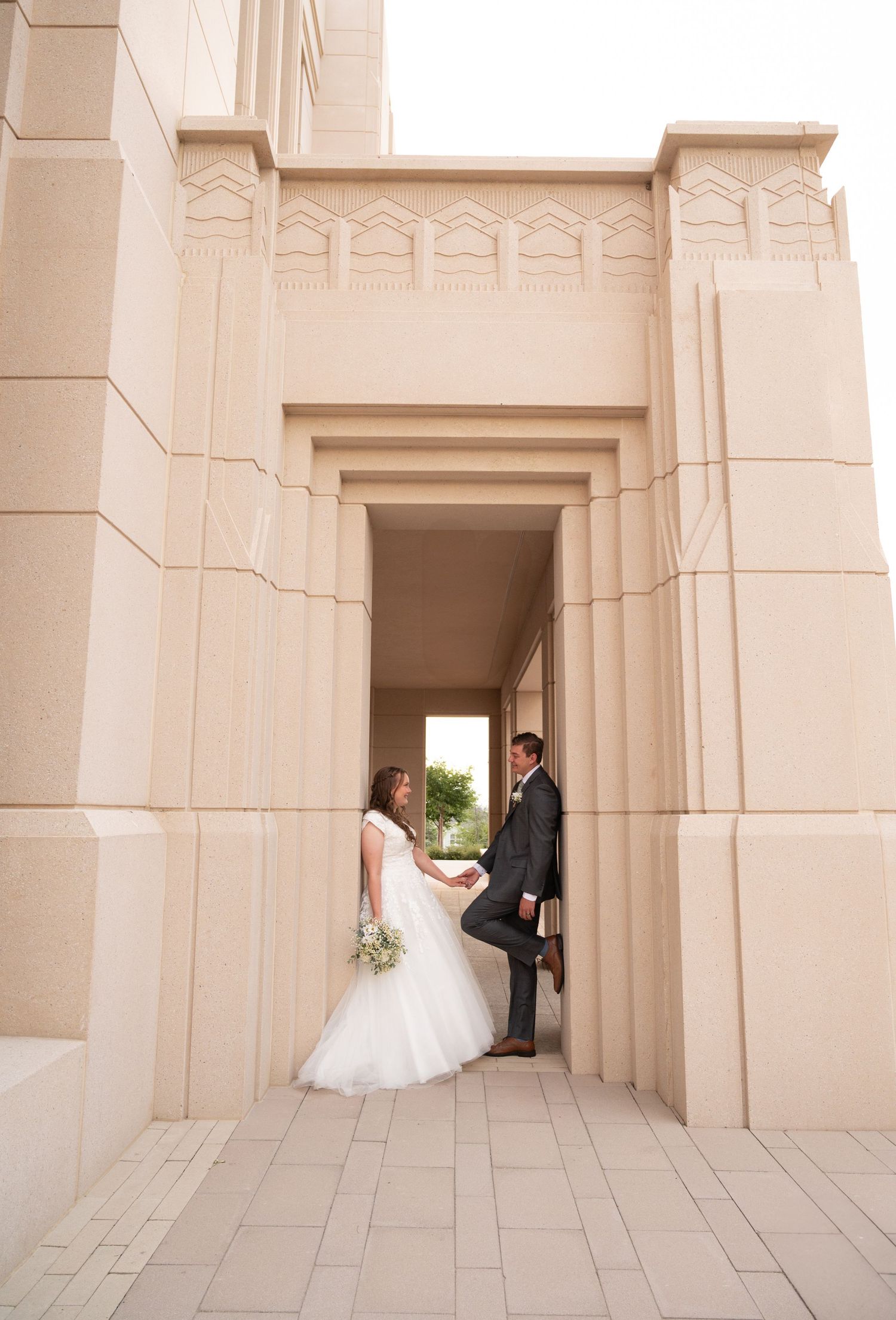 Wedding couple poses in elegant stone archways of a grand building.