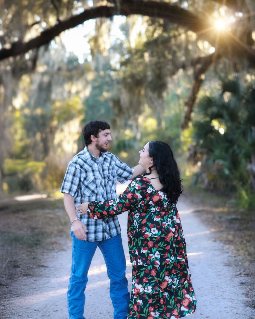 A couple shares a tender moment together on a sunlit path surrounded by trees during a romantic outdoor photoshoot.