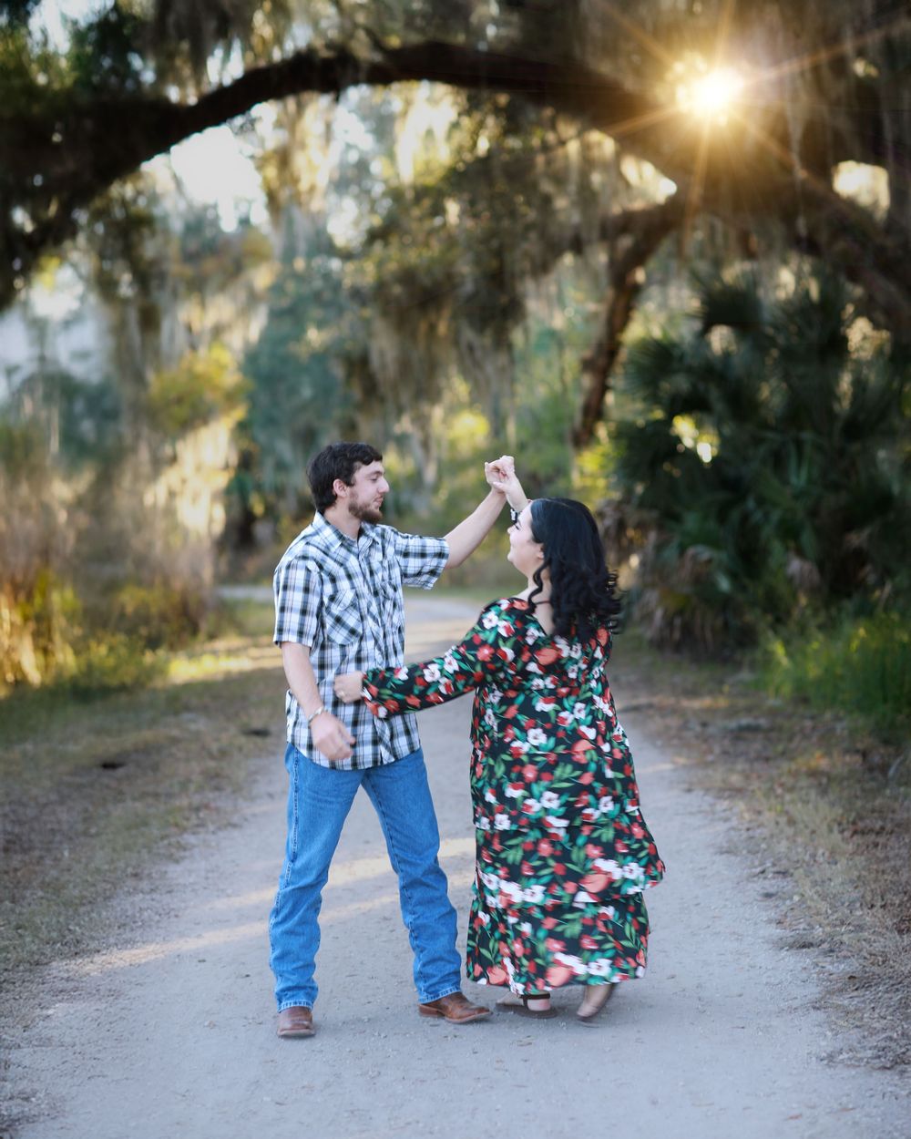 A couple dances together on a sunlit path surrounded by trees during a romantic outdoor photoshoot.
