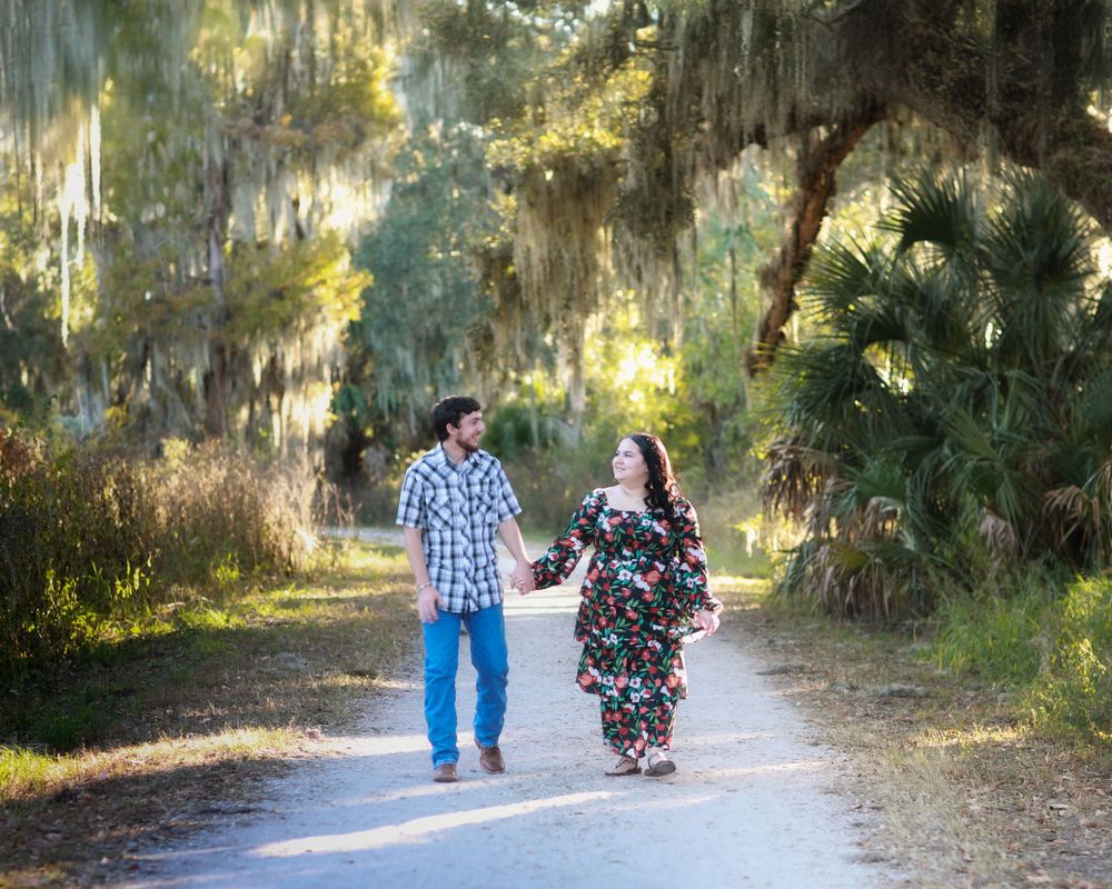 Two people walking hand in hand down a scenic tree-lined dirt path on a sunny afternoon.