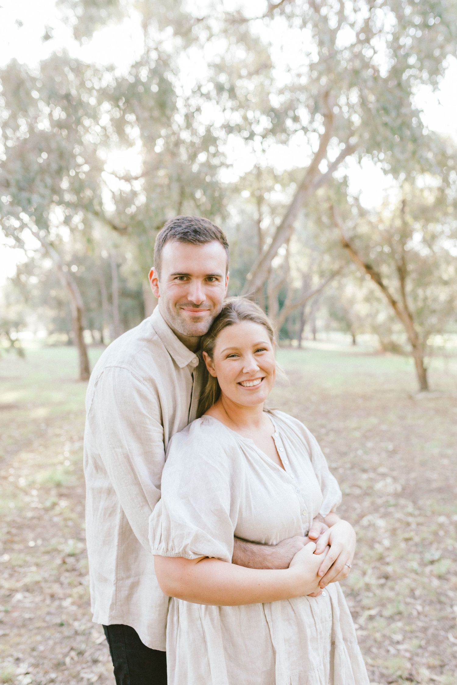A couple outdoors embracing in a romantic pose among eucalyptus trees in a dreamy sunlit setting.