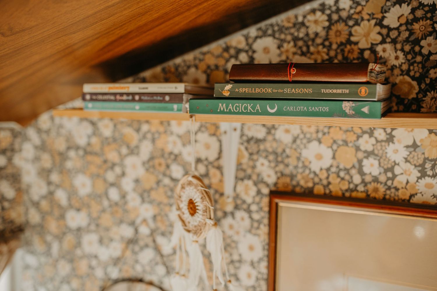 A row of ornate hardcover books displayed in front of a floral wallpaper backdrop.