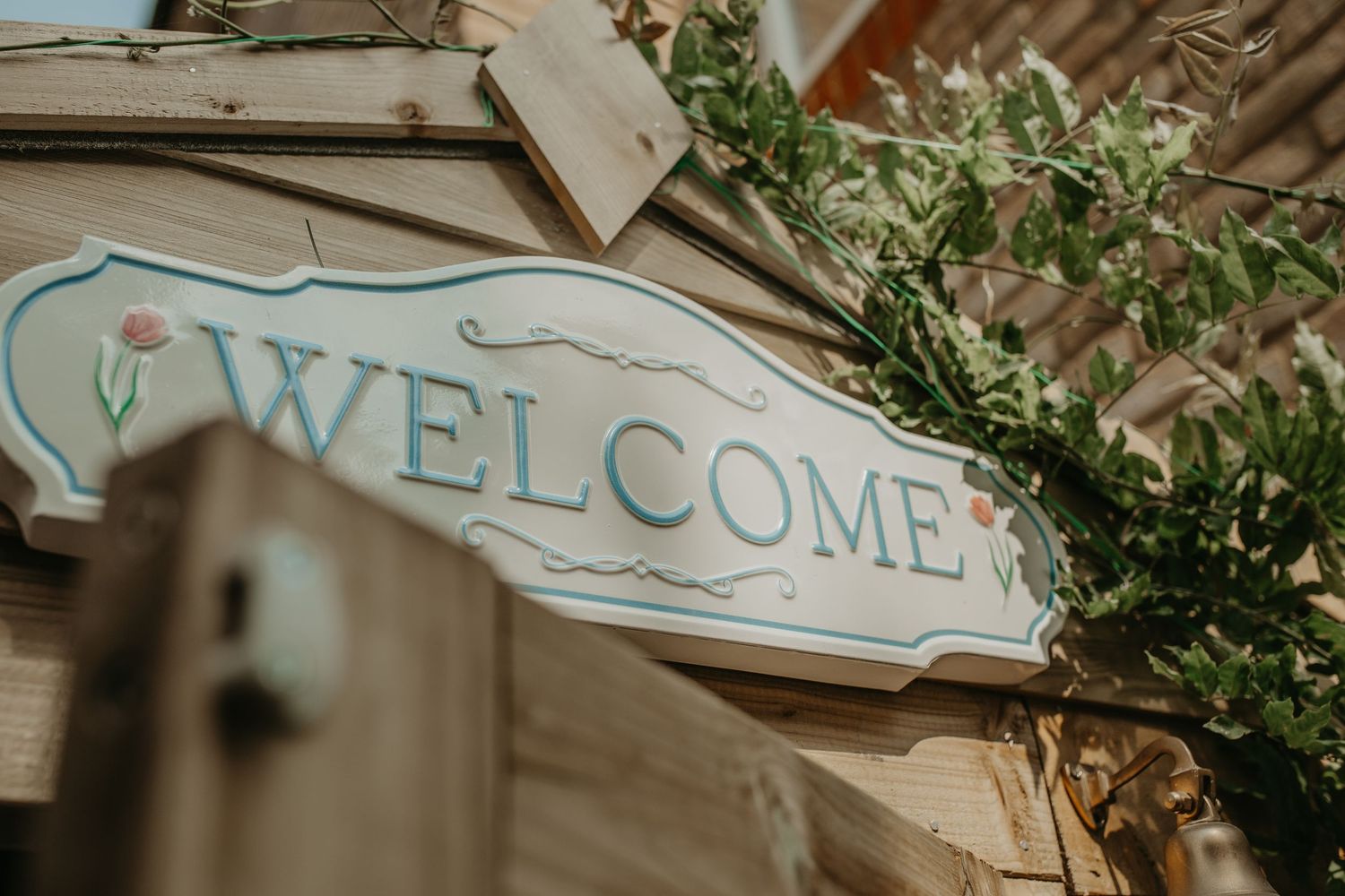 A vintage-style beach cottage signage with welcome lettering features distressed blue and white colors and seashell motifs.