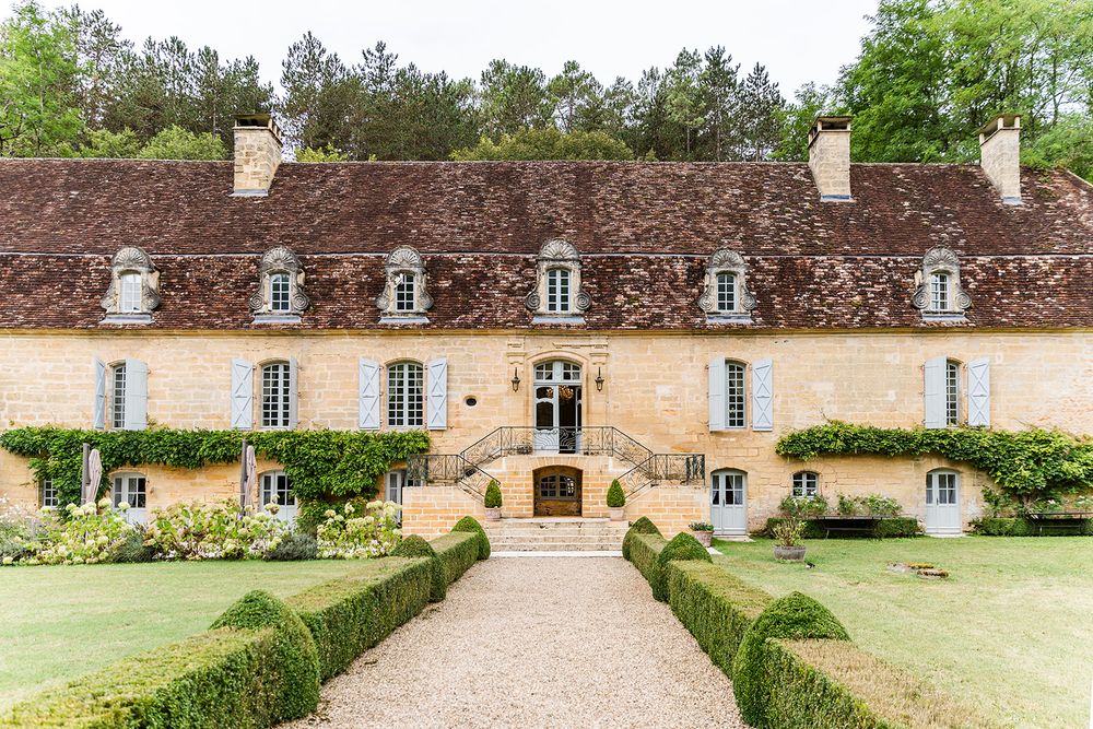 Beautiful French country manor house with dormer windows and manicured hedges along a gravel pathway.